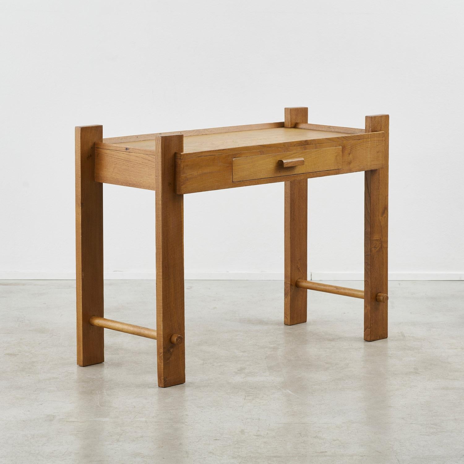 A simple wooden writing desk or dressing table with a drawer to the front, enhanced by the interesting jointwork and visible grain. There is a wooden lip at the edge of the working surface, ensuring papers, books or rolling lipstick remain at hand.