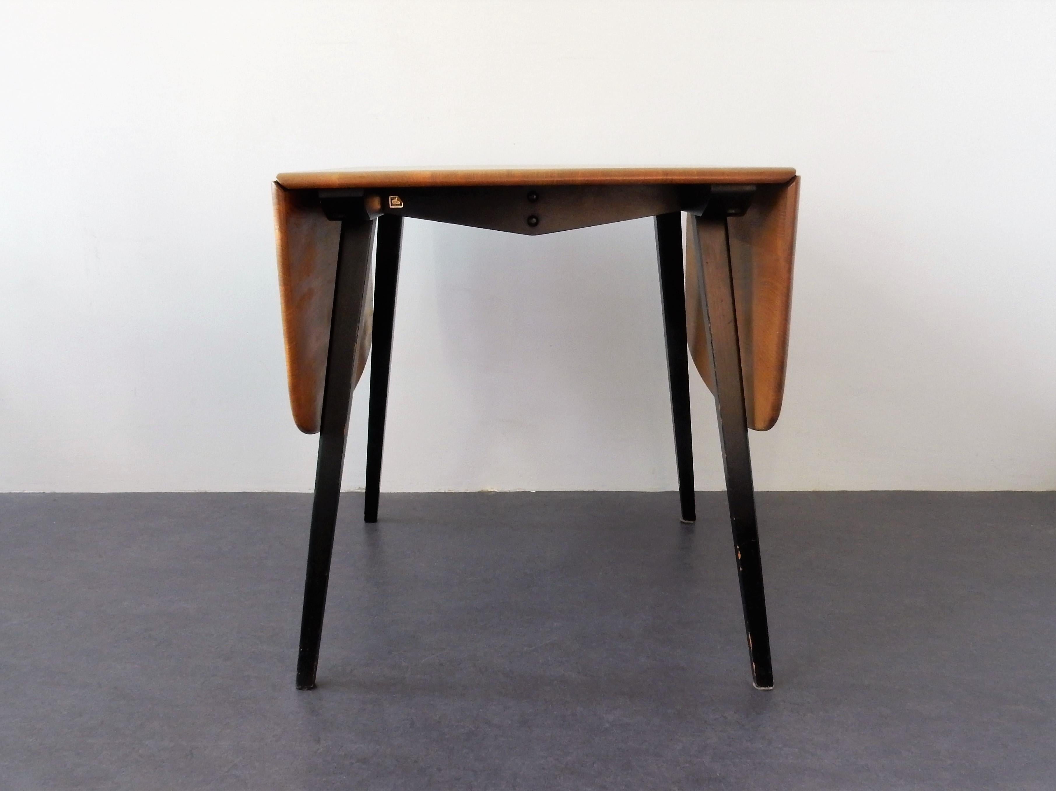 This vintage drop-leaf table was designed by Lucian R. Ercolani and manufactured by Ercol England during the 1960s. This double drop-leaf table consists of a solid wooden top on tapered black lacquered wooden legs. It is labeled by the