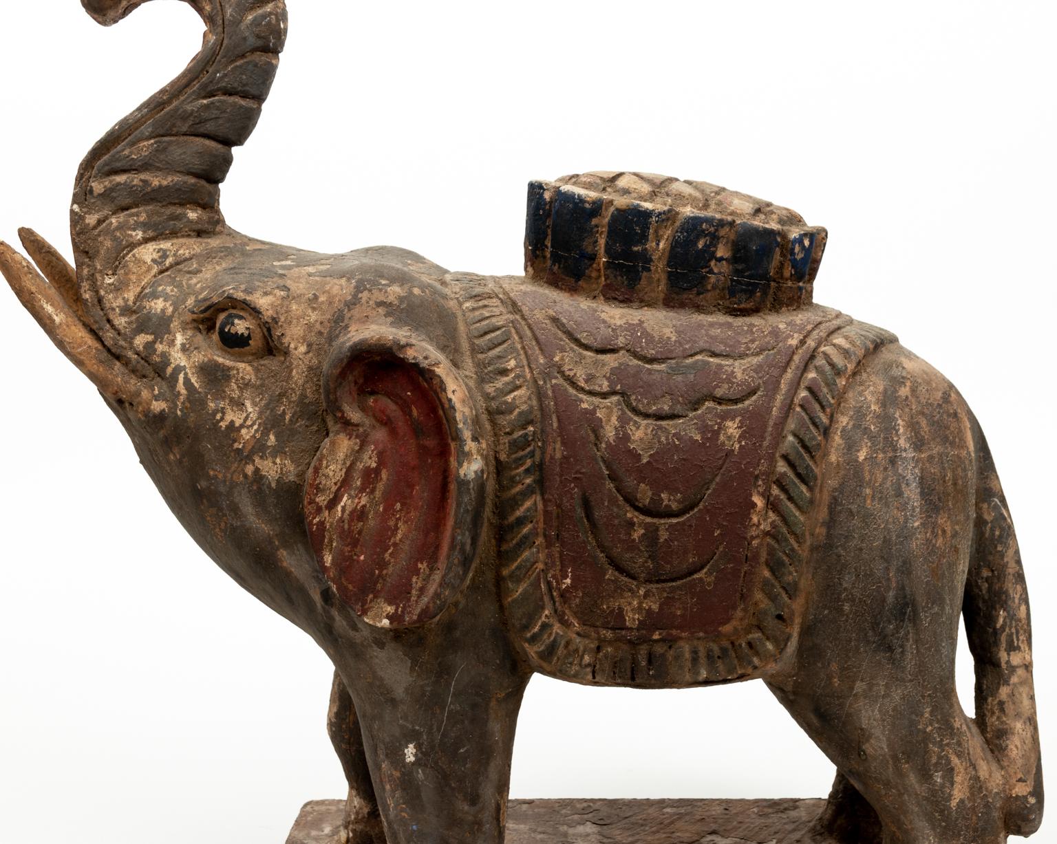 Carved and painted wooden elephant statue with raised trunk. Please note of wear consistent with age including distressed finish, minor paint loss, chips, and wood loss.
