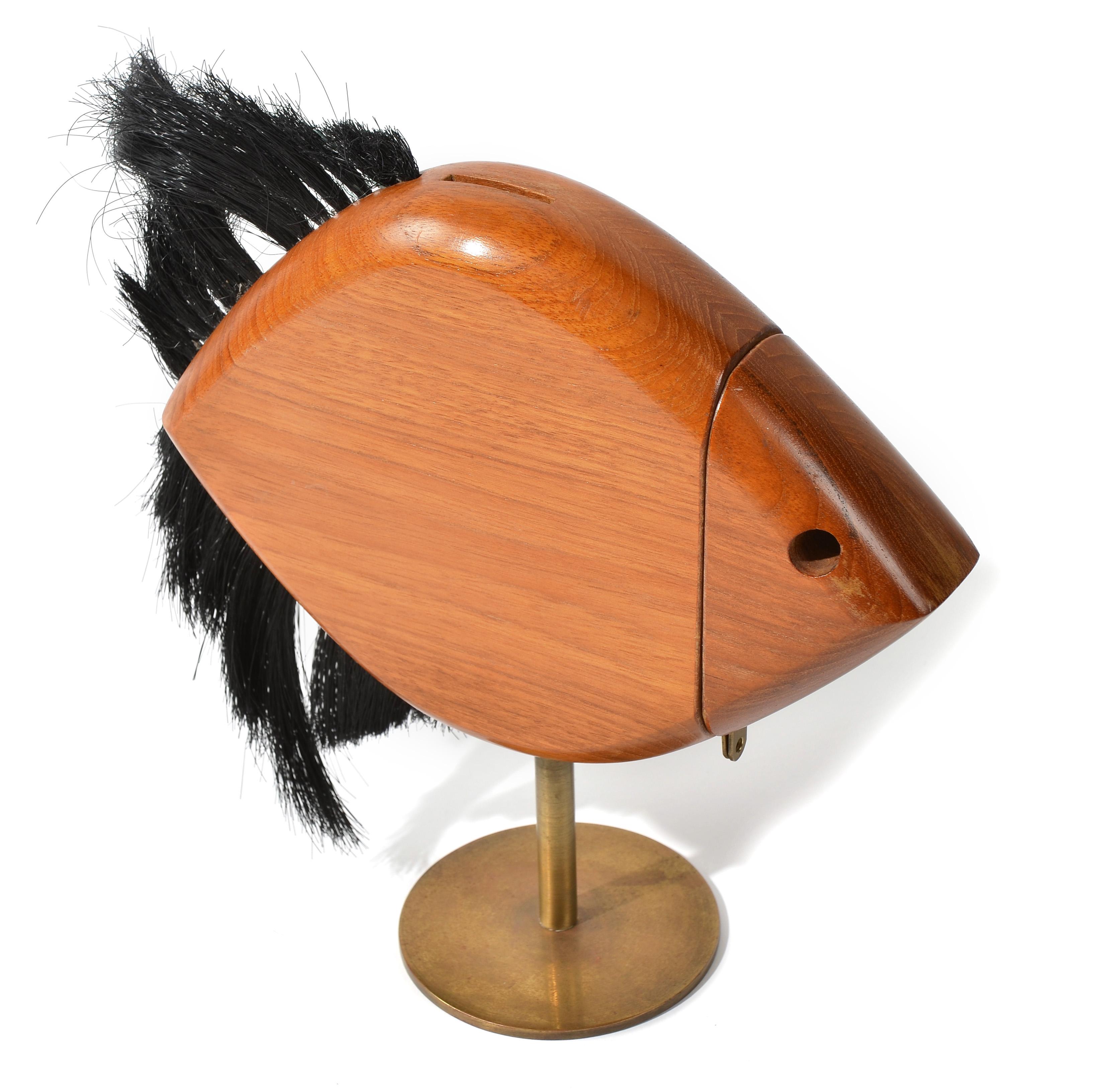 A wooden savings bank sculpted in the form of a fish designed by Carl Aubock. The black synthetic bristle fins and brass rod mounted form create an illusory swimming movement. The head is removable, to empty the bank, but can be locked with a small