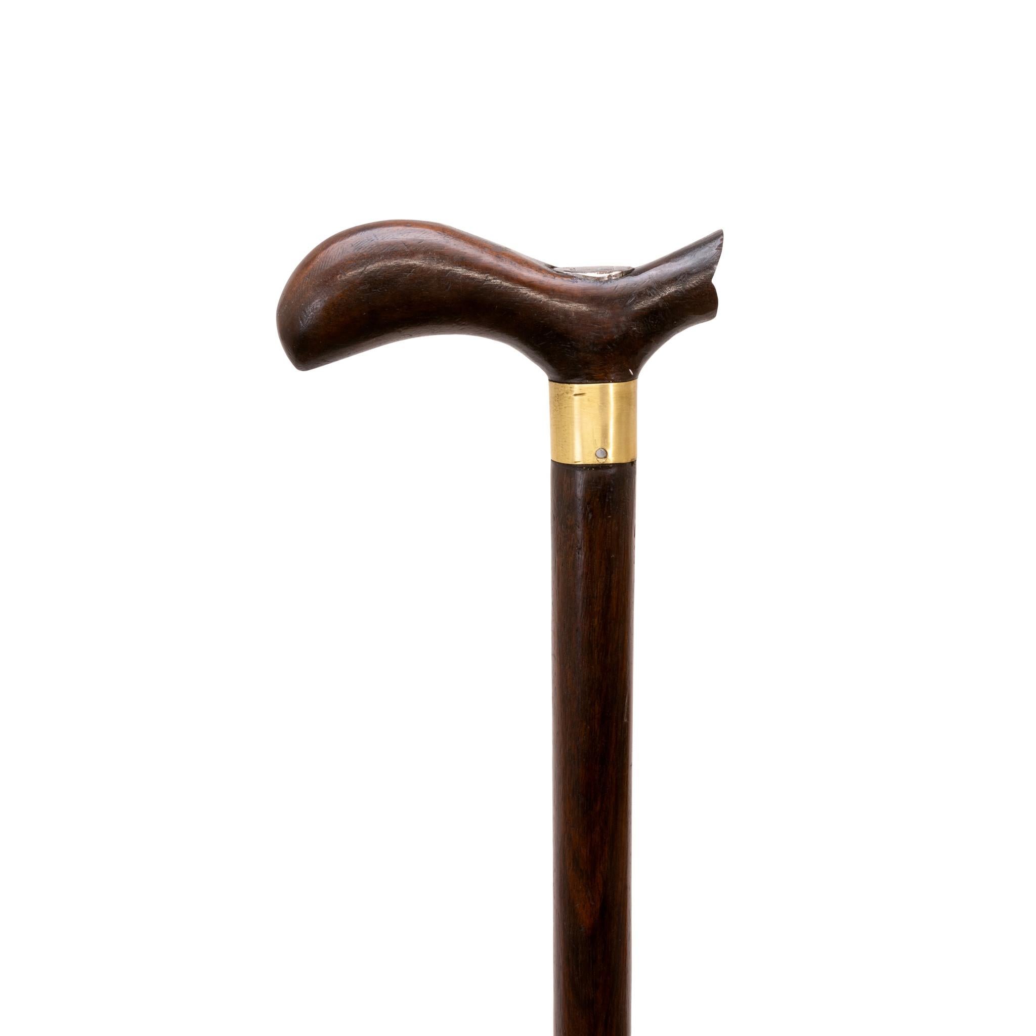 Bastone a scatto in legno della fine del XIX secolo. Manico in legno intagliato con attacco in metallo in cima, collare in ottone, asta in legno duro e nessuna ghiera. Questa canna deve essere colpita con forza per aprirsi completamente. Il bastone