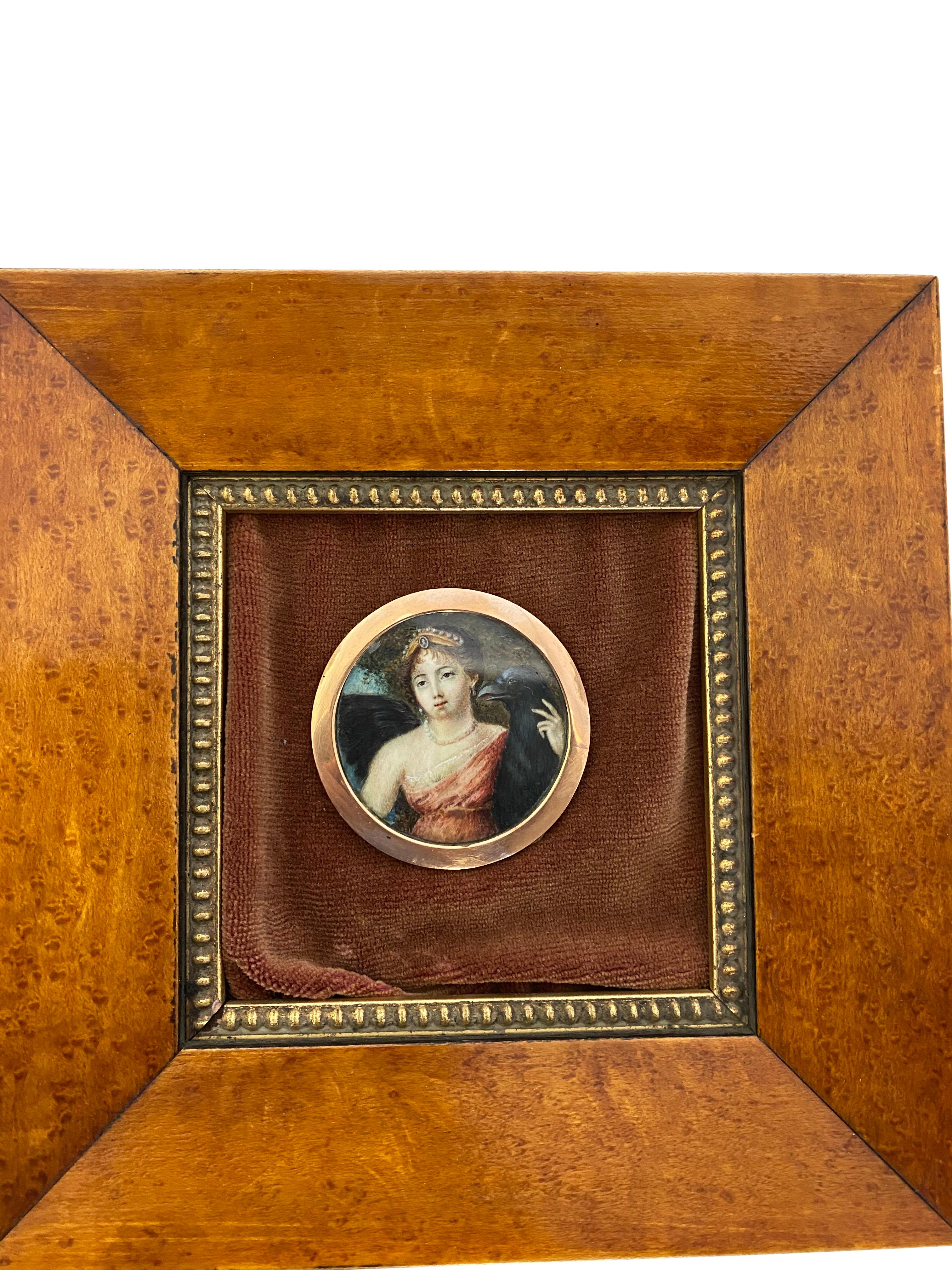 A rustic, wooden-framed picture on a hand painted porcelain panel of a young lady wearing an orange dress and braided hair, whilst holding onto a large black bird of prey. Inlaid with fabric and a metallic inner-frame.

Dimensions (cm):
H 24, W