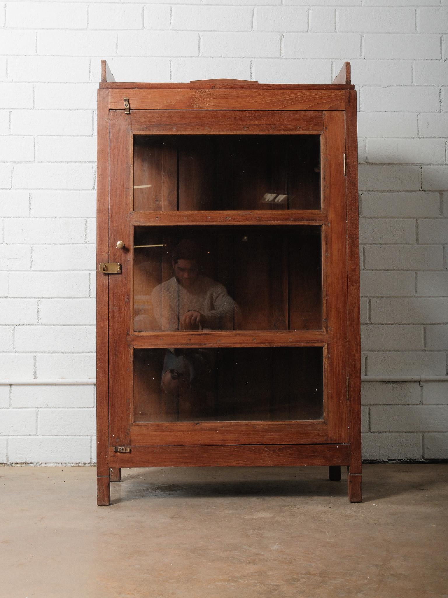 Questa bella vetrina in legno mostra il calore e l'autenticità dell'artigianato indiano del XX secolo. Costruito in legno massiccio con tre finestre in vetro a pannello intero sulla parte anteriore e ulteriori pannelli in vetro su entrambi i lati,