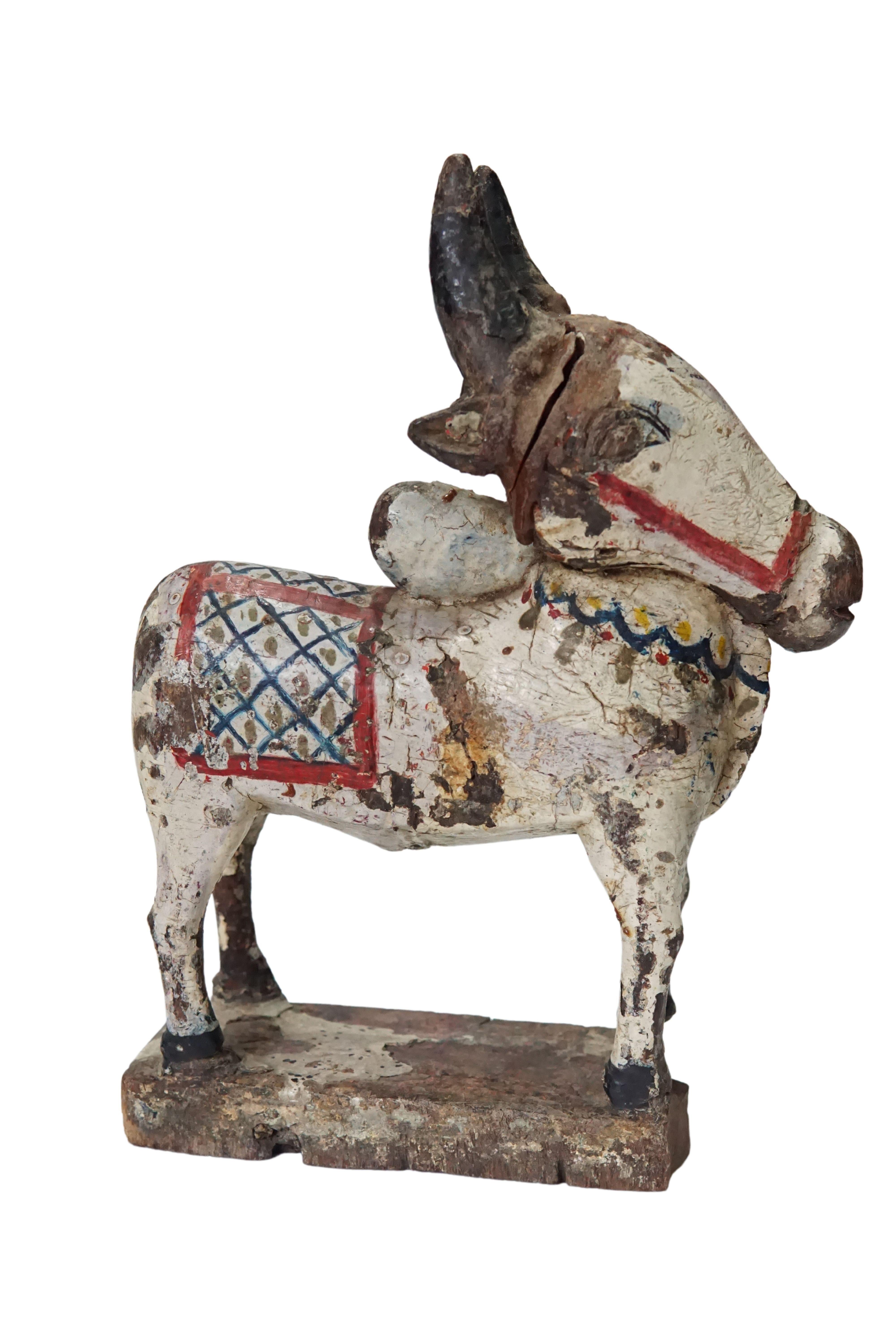 A visibly old hand-carved Nandi Cow from India. This wood sculpture features a wonderful age related patina and has been hand-painted with a mix of white and bright colours. Nandi according to Hindu mythology is a protecter of the god Shiva. Nandi