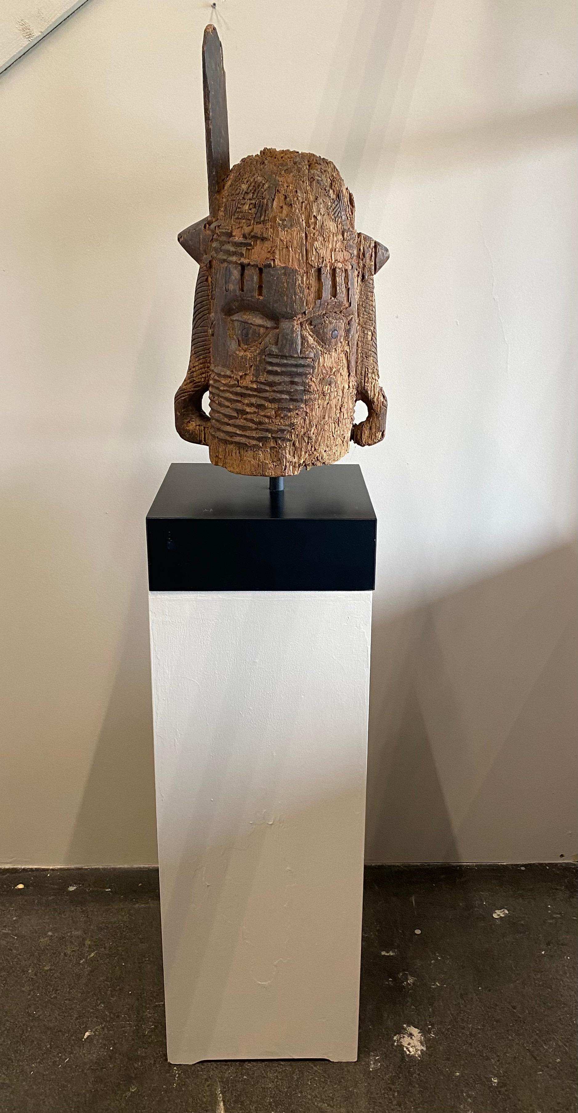Carved from reddish brown hardwood, the hollow form rises from a cylindrical neck, the lowest part being a rounded base, then surrounded by diagonal sections. The neck is surrounded by nine rows of coral beaded necklaces (odigba) that extend to a