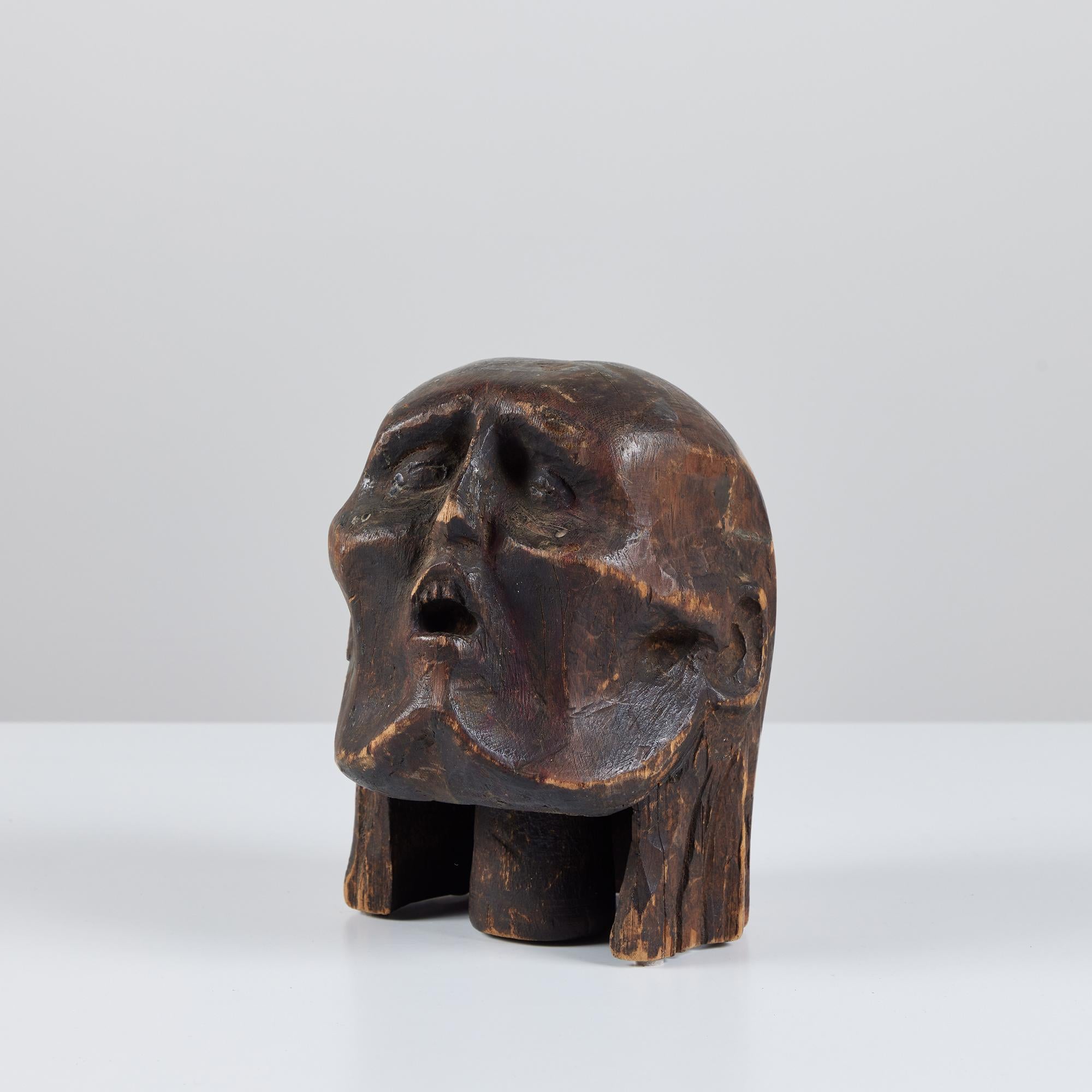 Hand-carved wooden head displays two varying wood tones throughout. The piece has been patinated to the point of perfection. Carved from a solid piece of wood this piece features a gaunt appearance and sunken eyes with partially open