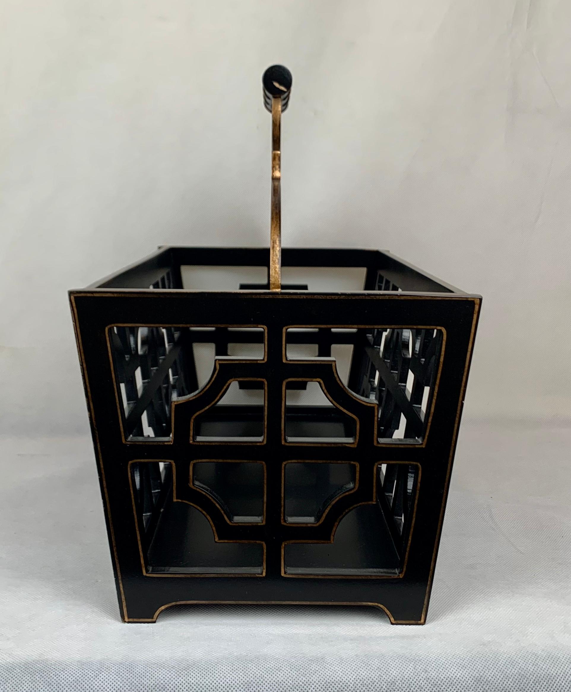 Black wooden magazine rack having cut out fret work panels with gilt edging. There are two long sections with a scalloped divider topped by a faux bamboo handle.
H-11.5