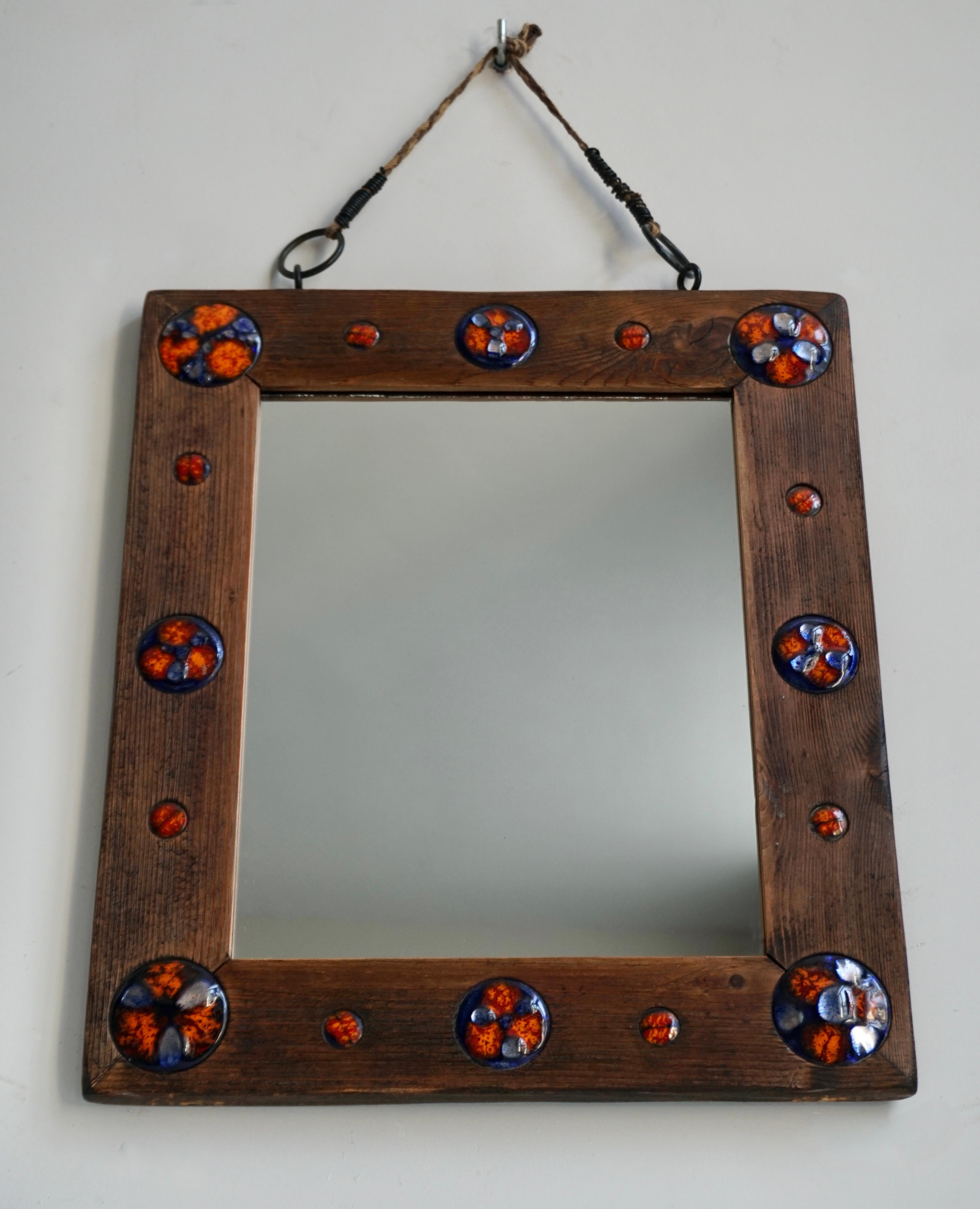 Wooden mirror with enamel decorations.

A rectangular wooden mirror with colored enamel decorations hanging from a rope.