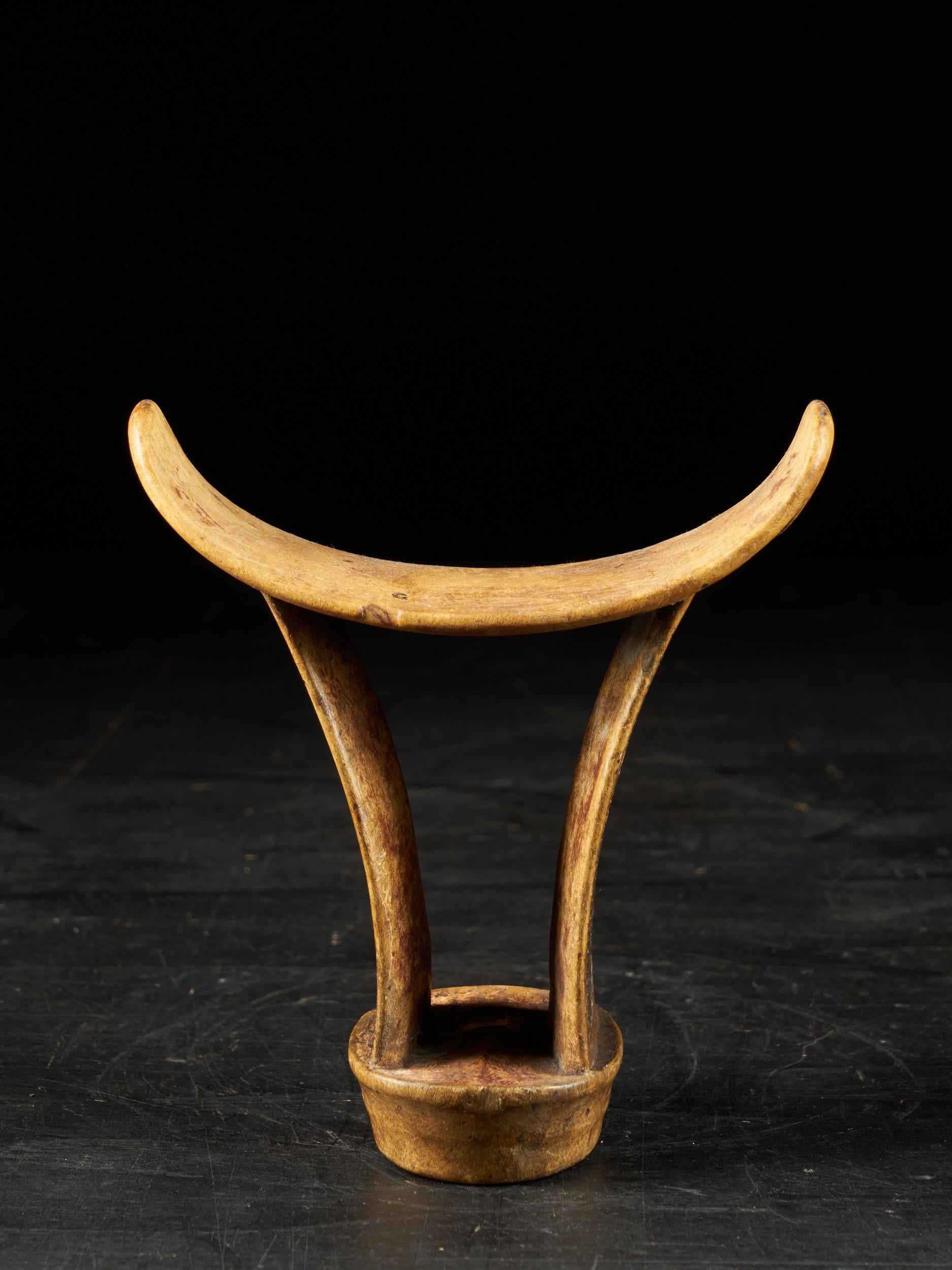 A wonderful headrest from the Karamojong People of Uganda in eastern Africa. It is made out of one piece of wood with the legs having a nice bend shape, supporting on a circular block. The neckrest is decorated at the sides with beautiful abstract