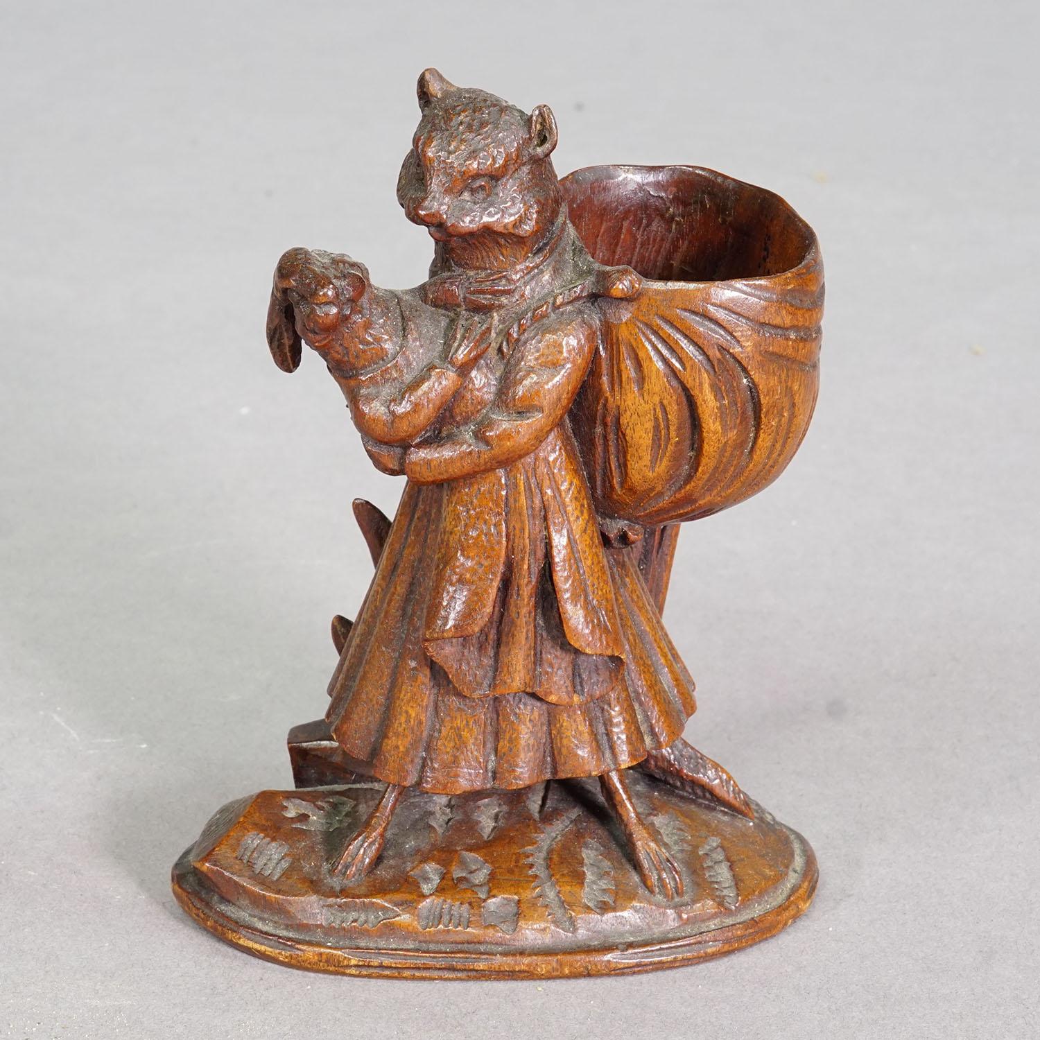Wooden Sculpture Cat with Rabbit Handcarved ca. 1900s

A hand-carved wooden sculpture depicting a cat in a flowing robe gently holding a rabbit in her arms. She carries a large, draped sack on her back. Depictions of animals in human form are among