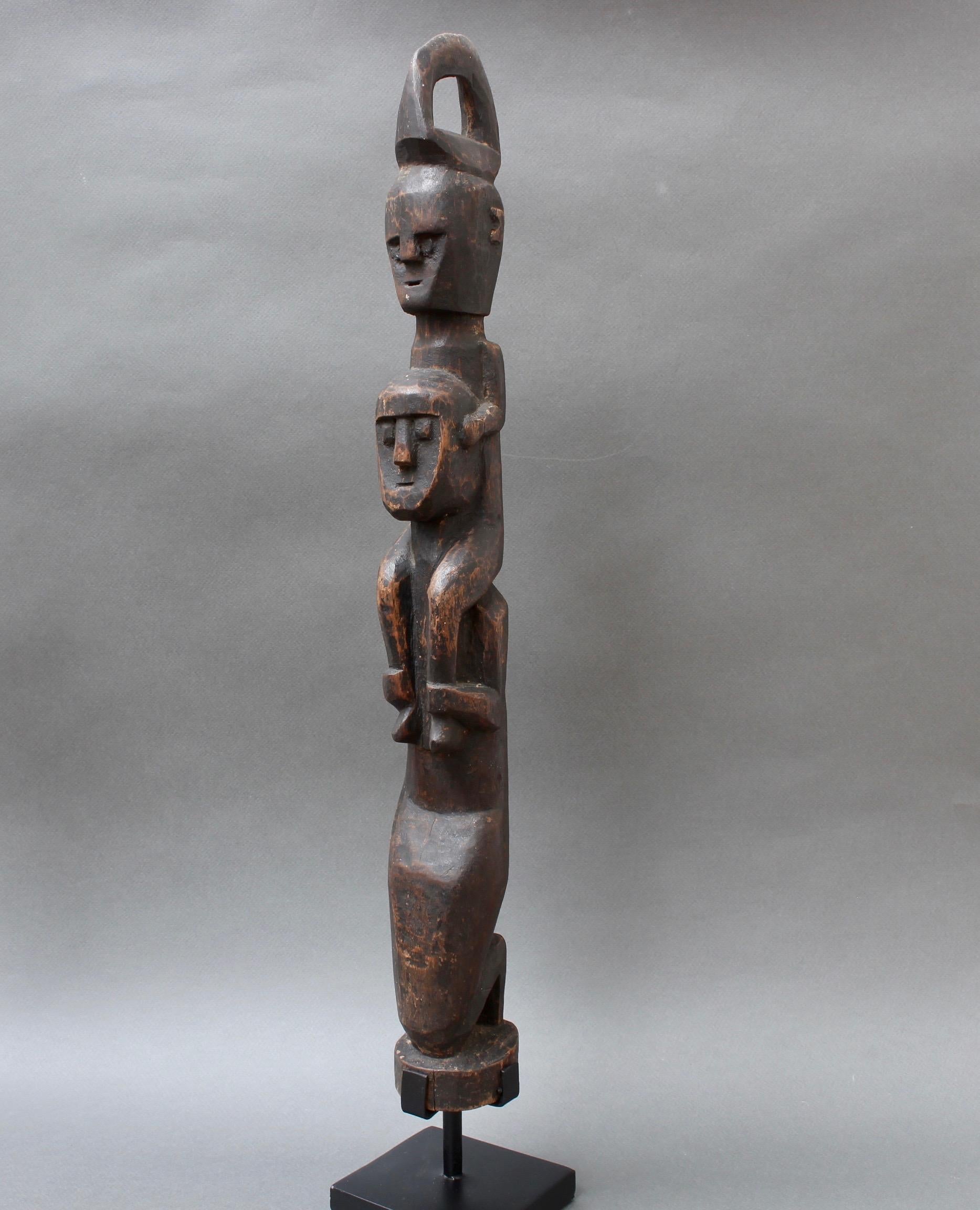 Wooden carving / sculpture of kneeling wooden figure with another on the shoulders from Timor, Indonesia (circa 1970s). The piece is in fair vintage condition commensurate with age and use and is situated on a contemporary stand. There is an aged,