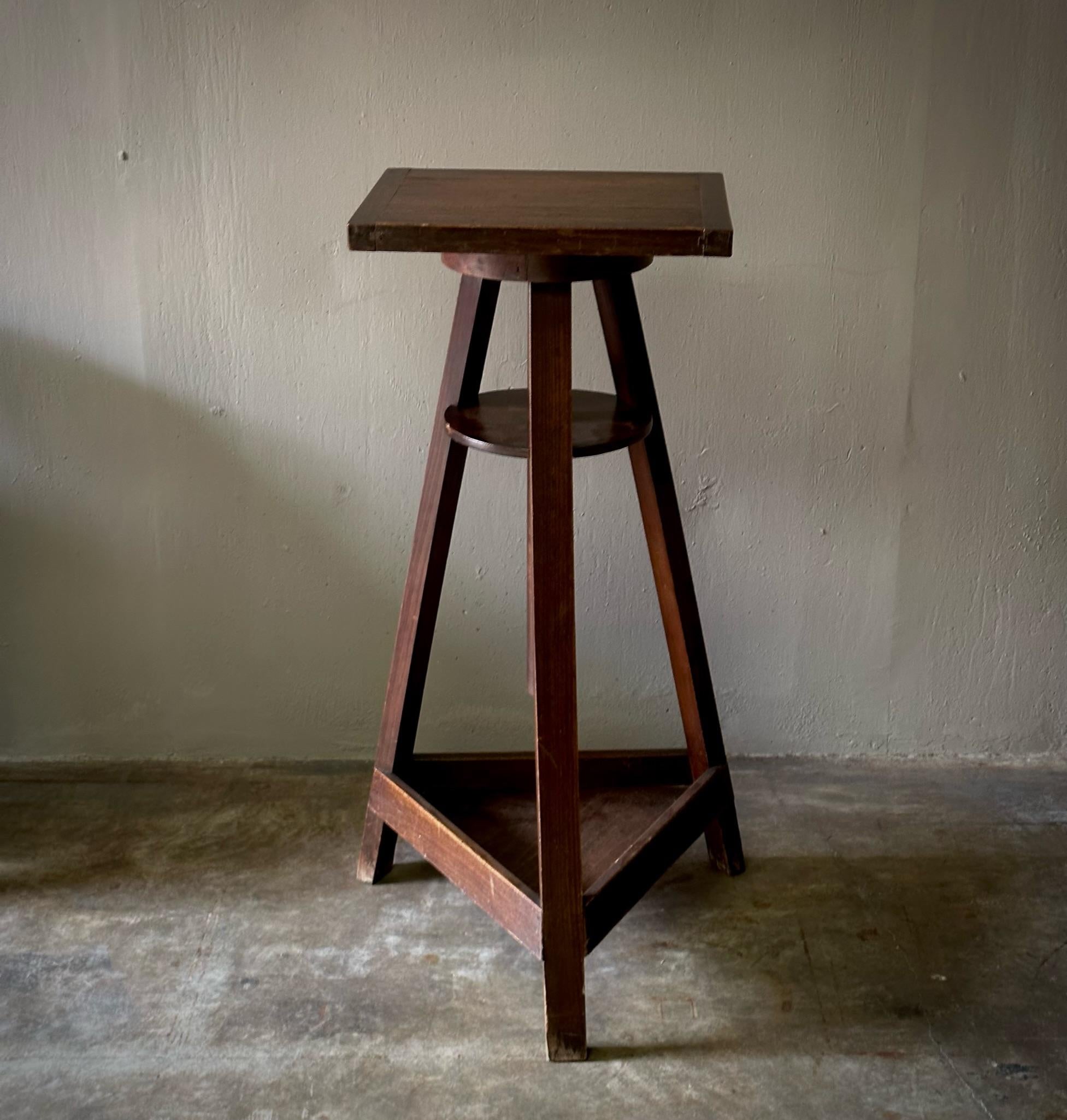 Wooden artist's pedestal produced for turn of the century French sculpture studio. Features small square top and tripod base with two shelves, one circular at the top and one triangular at the bottom. A quirky yet subdued piece, perfect for the