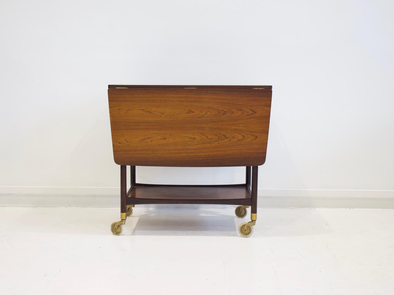 Ludvig Pontoppidan serving cart made of wood with two cloves, top covered with black Formica. Two underlying shelves and a drawer. Set on four brass wheels.
Measurements when the table is open: H 71 cm, W 113 cm, D 75 cm.