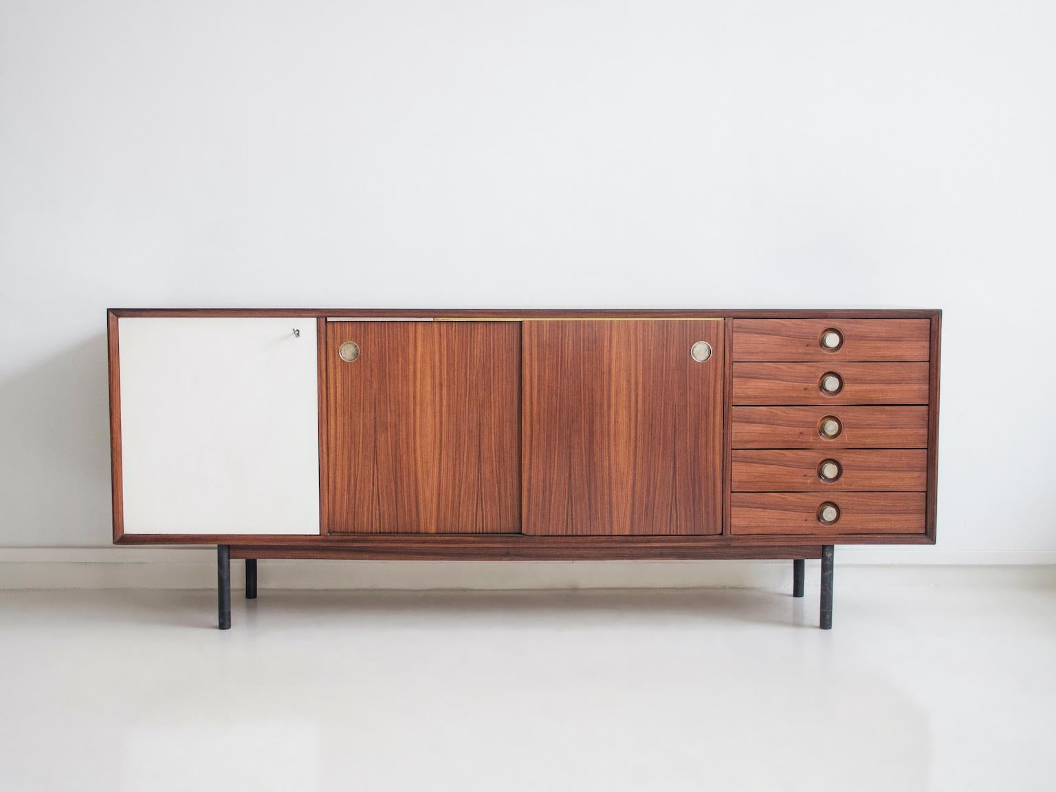 Aparador largo de madera fabricado por Faram en Italia, años 60. De madera dura chapada, puertas correderas por ambos lados de laminado blanco y madera, patas de tubo de acero cepillado con virolas de madera maciza. Asas de metal.