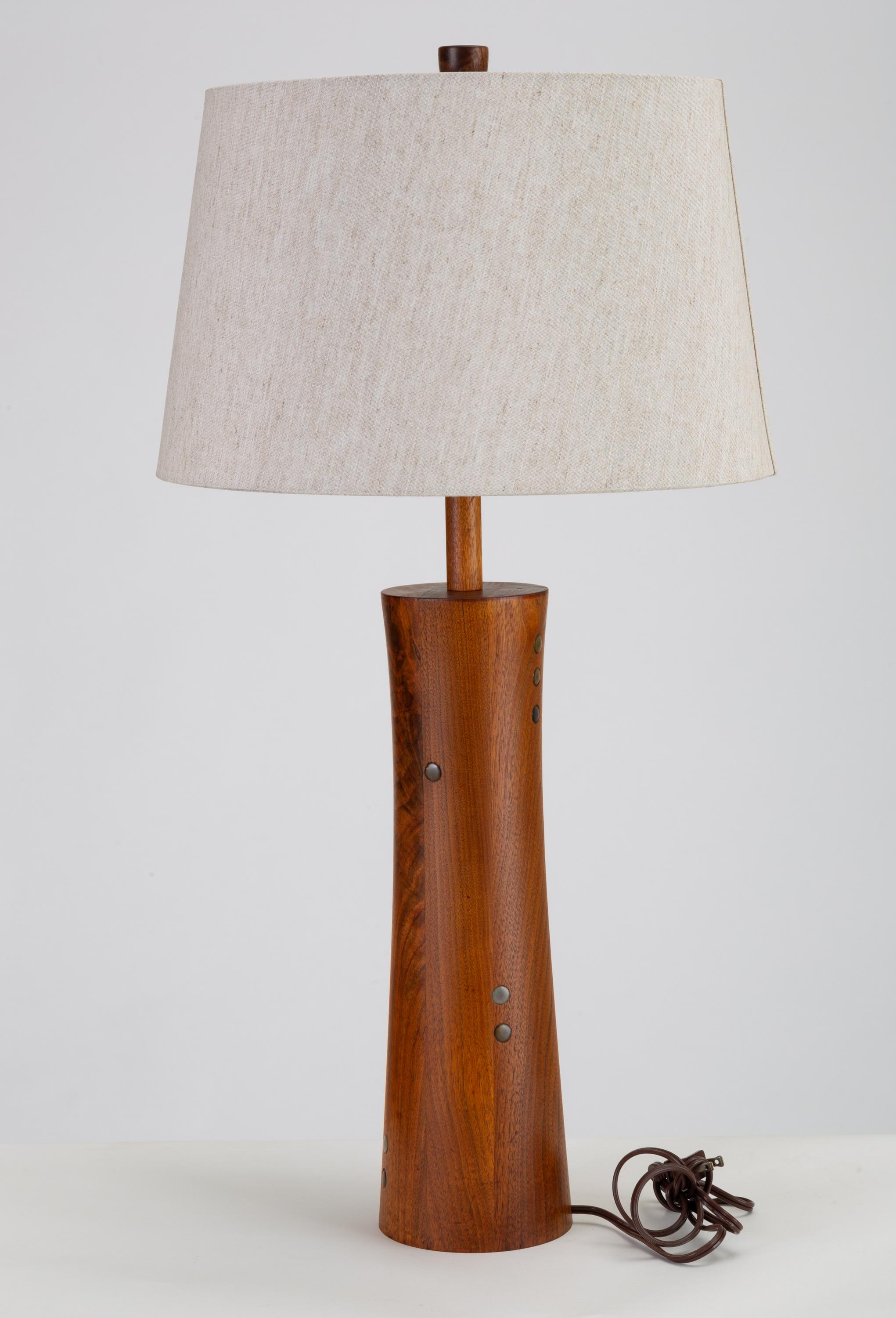 A lathe-turned walnut lamp from Midwestern ceramics artists Gordon and Jane Martz for their company Marshall Studios. The table lamp has a slightly hourglass shape, and is inlaid with small ceramic coins in earth tones. A study in attentive