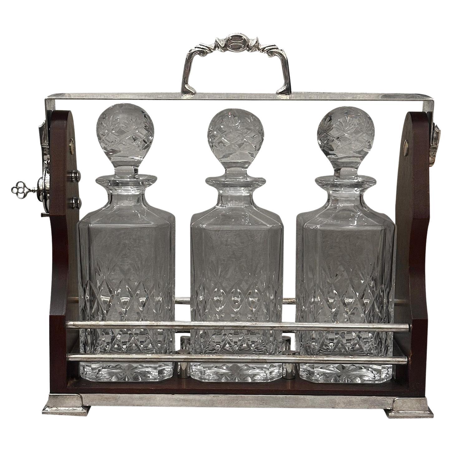 This English tantalus consists of three square-shaped cut crystal decanters, each with a matching stopper. The glassware is in excellent condition, featuring diamond-shaped engravings on the surfaces that add an elegant decorative touch. The round