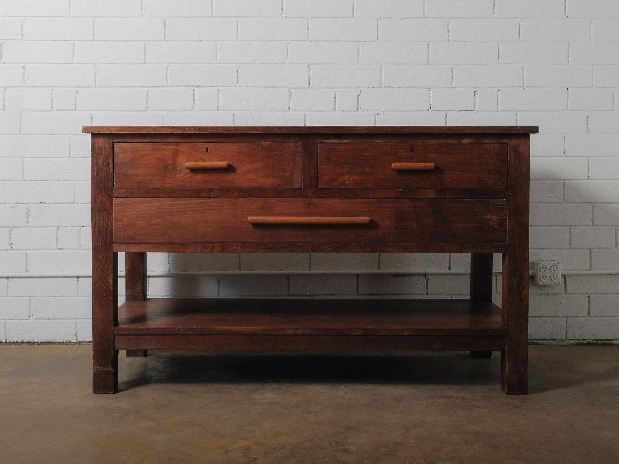 A sturdy wooden console built with clean lines and practical proportions. The wide three-drawer front features simple rounded pulls and visible joinery, highlighting its straightforward construction. The top shows natural grain variations and worn