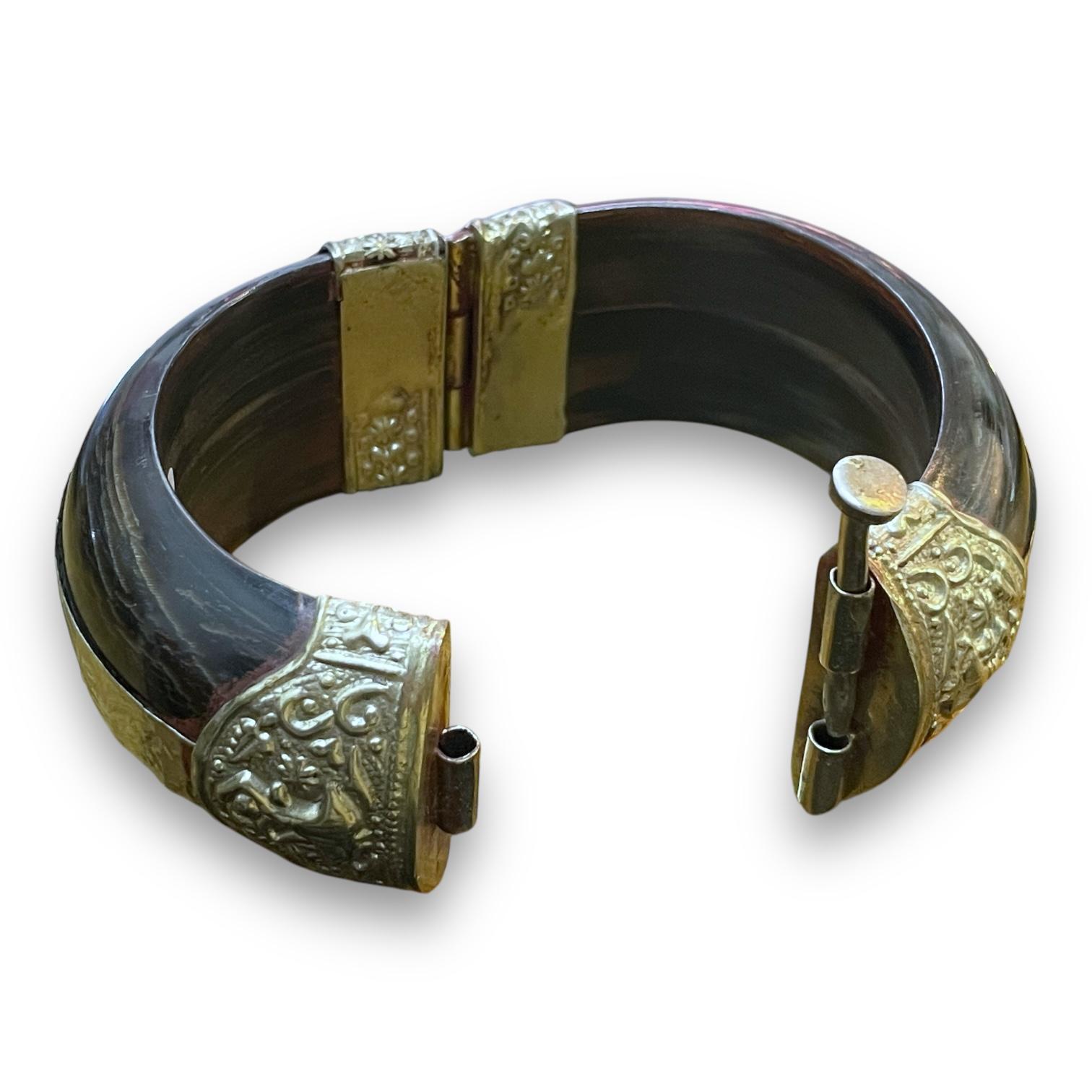 Esta pulsera presenta un diseño llamativo con intrincados grabados en tono plateado sobre una base oscura y pulida. Los detallados motivos florales añaden un toque de elegancia.