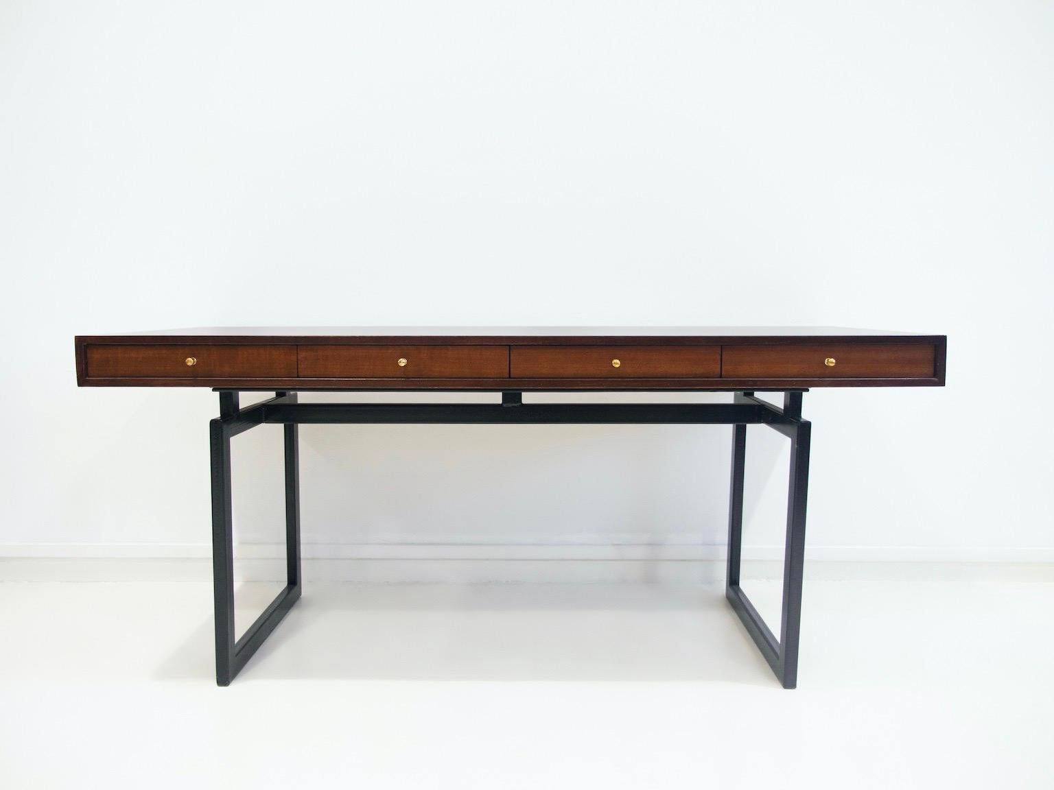 Large desk veneered with dark wood, front with four drawers with gold-colored pulls. Legs of black lacquered metal. 