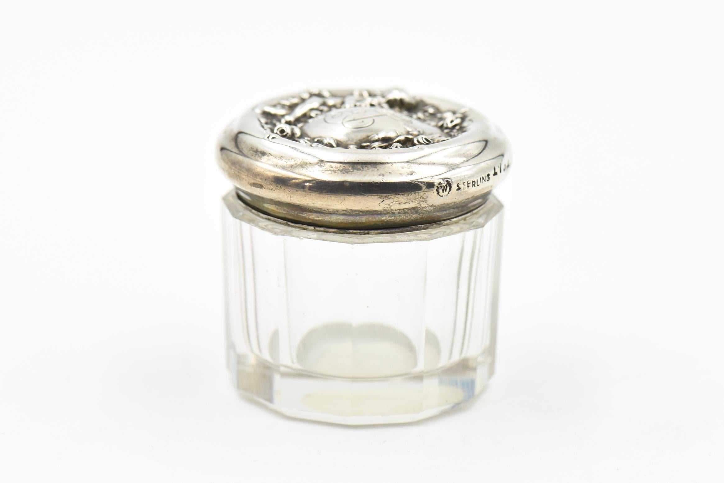 Sterling silver and beveled crystal dresser jar from the Art Nouveau Era, made by fine American silver maker, Woodside. The jar is features a child hugging flowers on the side of a floral wreath. The jar measures 1.5