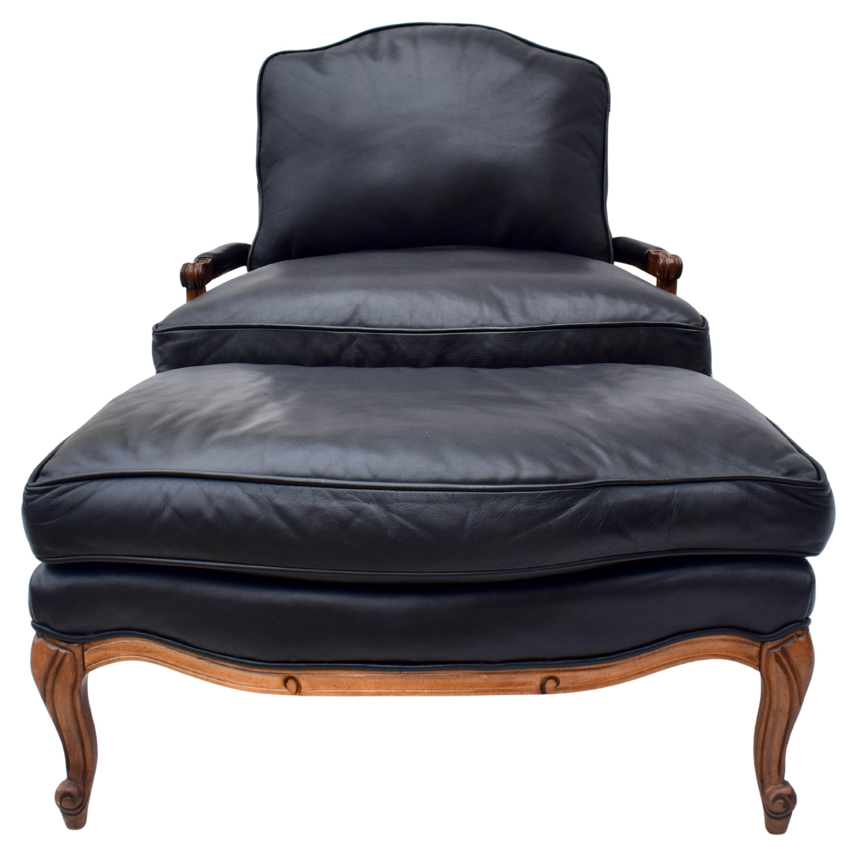 Supple Aniline black leather club chair and ottoman of generous proportions with warm contrasting carved walnut frame, arms, and legs. Ottoman dimensions:  22