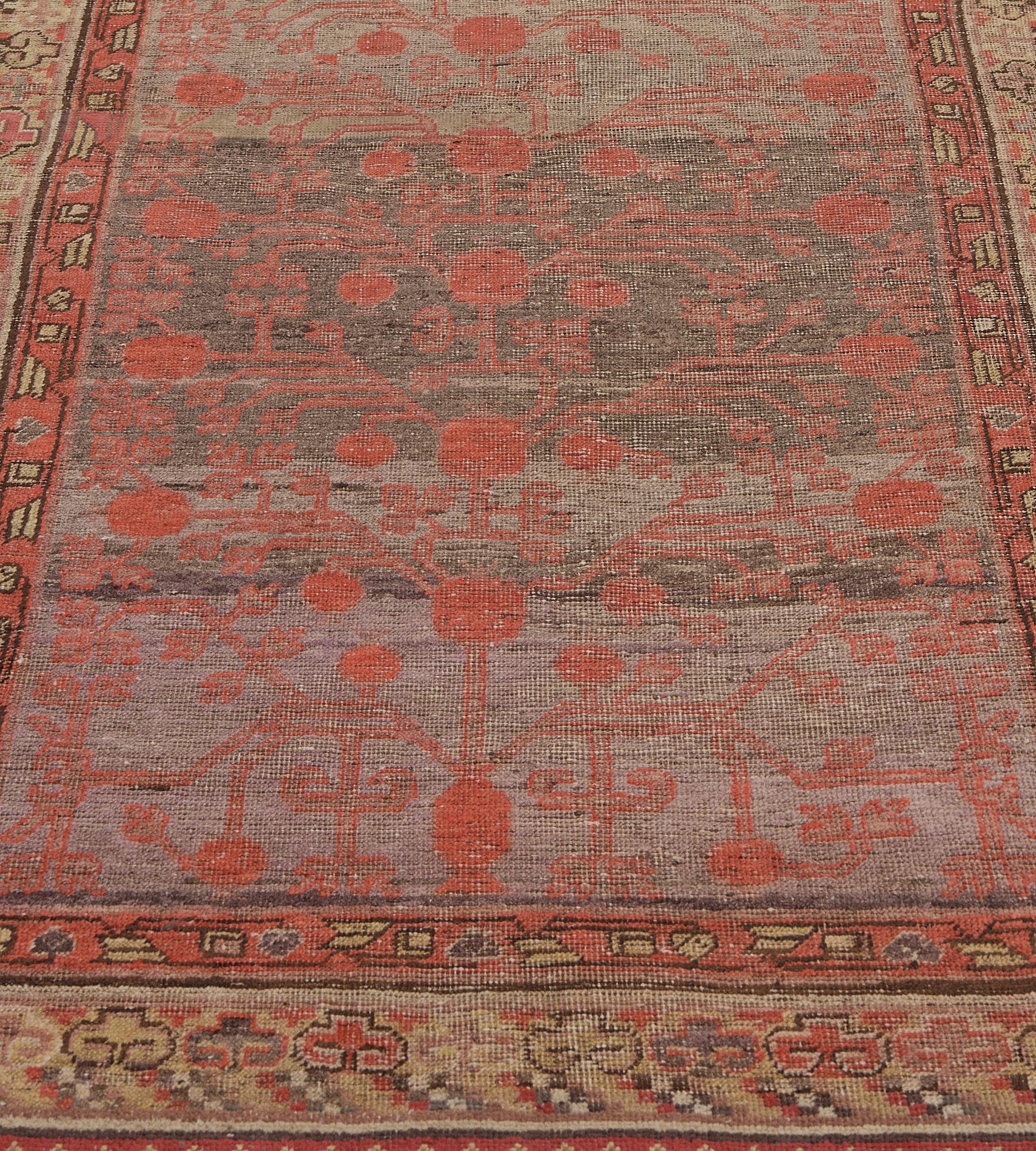 This antique, circa 1900, Khotan runner has a buff-brown and shaded aubergine-purple field with an overall delicate shaded terracotta-pink pomegranate vine, in a broad cloud motif border with diagonal striped polychrome wind motifs between shaded