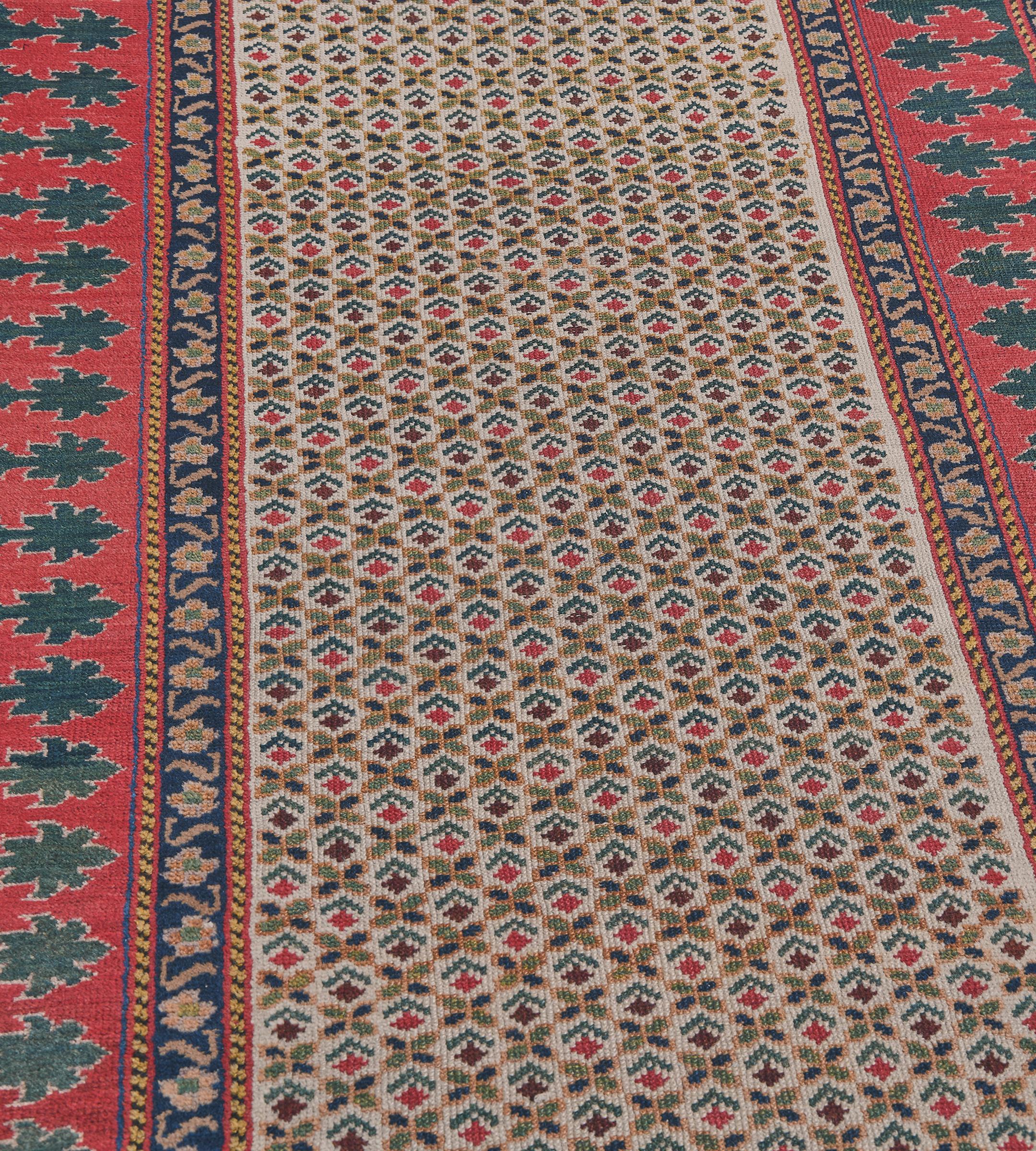 This antique, circa 1900, Caucasian runner has an ivory field with an overall design of delicate rows of polychrome plants alternating with quartered leaf motifs, in a bold tomato-red and sea-green reciprocal trefoil leaf border, between indigo-blue