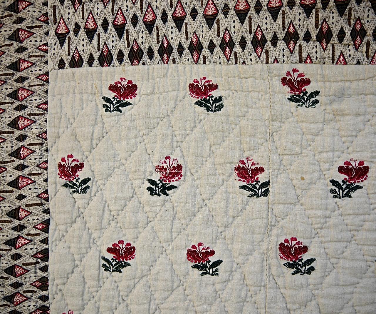 French late 18th century cambresine (wool woven on linen) quilt with a design of dark red and pink flowers with green leaves. Simply quilted with a diamond pattern. Bordered on four sides by a circa 1790s blockprinted design based on diamonds and