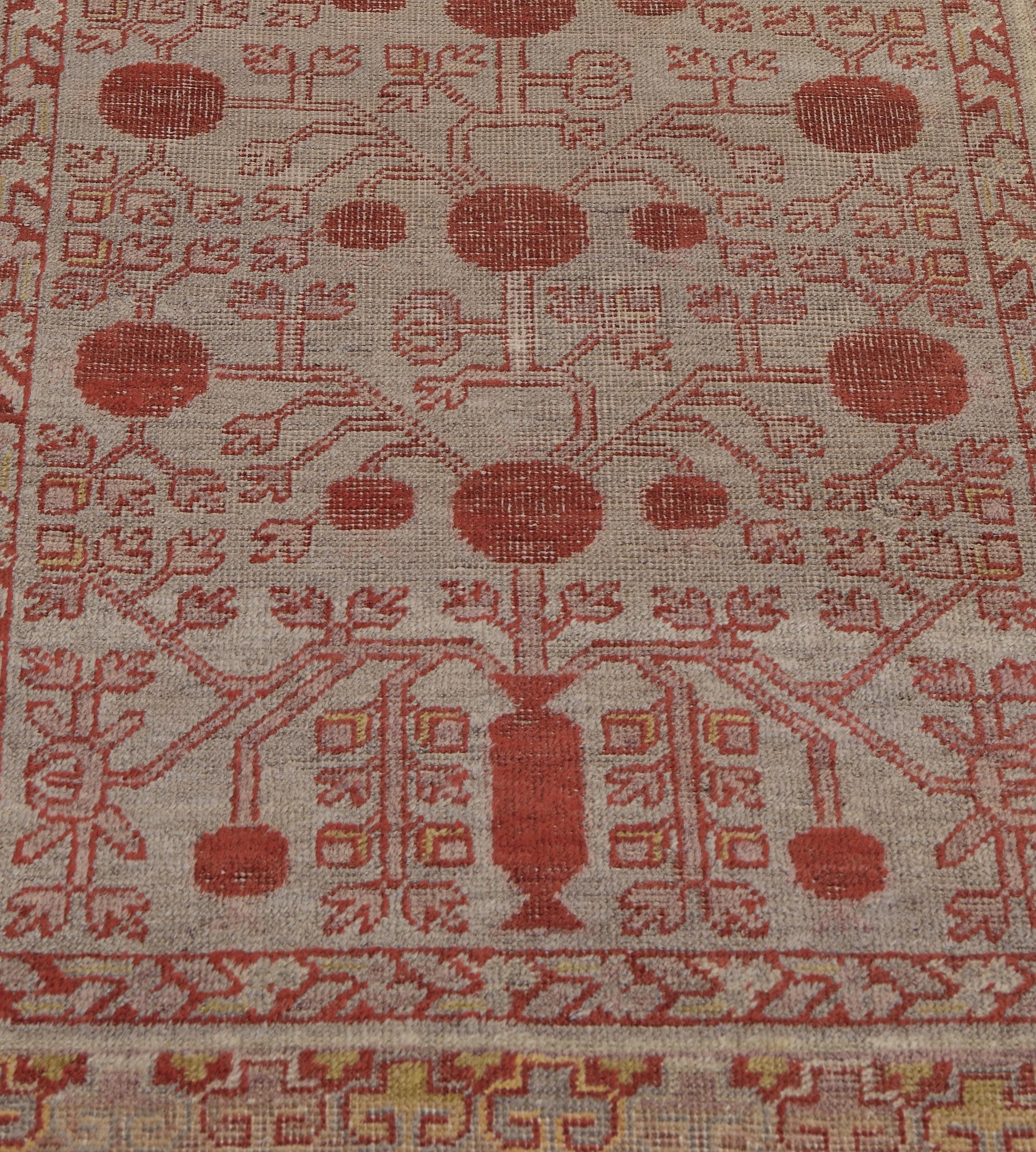 This antique, circa 1900, Khotan runner has a steel-gray field with a coral-red vase at each end issuing dusty-pink pomegranate and angular floral and serrated leaf vine, enclosed with a coral-red stripe with angular floral vine, in a border of
