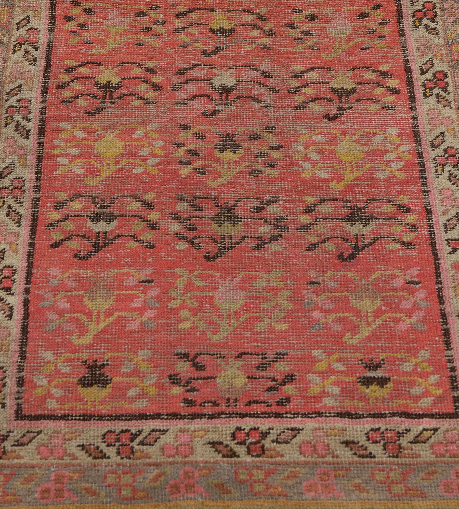 Cet antique chemin de table du Khotan présente un champ rouge corail parsemé de délicates gerbes florales brun chocolat et vert pistache autour d'un rondeau central bleu acier, entouré d'une bande ivoire de délicates gerbes florales, dans une