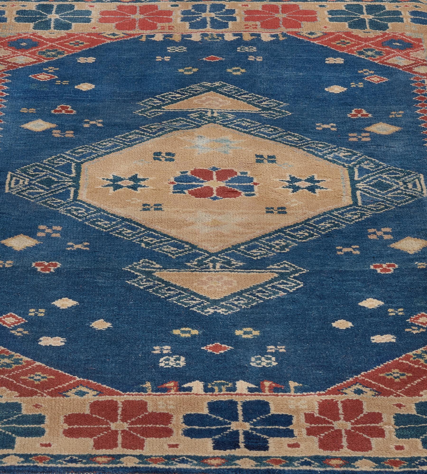 This traditional hand-woven Turkish rug has a deep blue field enclosing a central medallion surrounded by petit floral sprays, in a red and blue stylized floral border, with an outer blue stripe featuring polychrome diamonds.