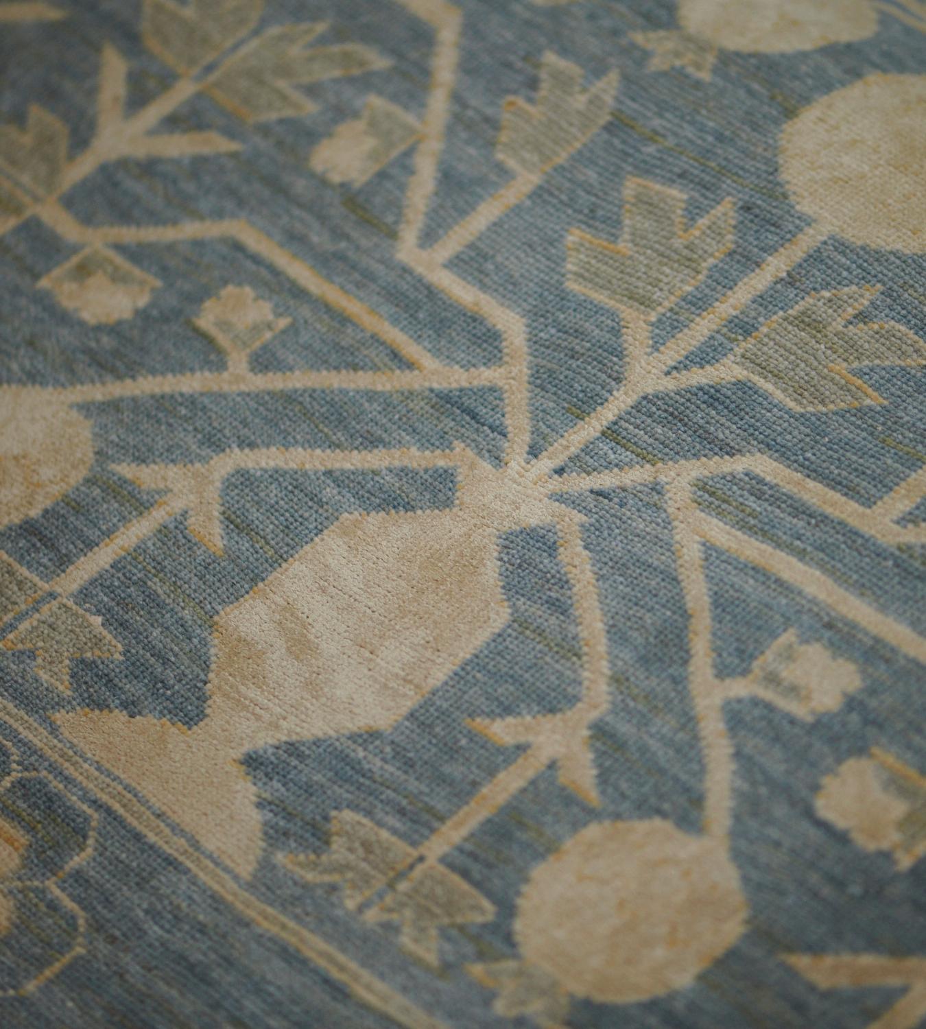 Dieser Khotan-Teppich aus Wolle und Seide zeigt ein schattiertes blaues Feld mit einem Gesamtmuster aus buff-braunen Granatäpfeln, die durch eckige Blattranken miteinander verbunden sind, in einer doppelt gestreiften Bordüre, wobei der innere