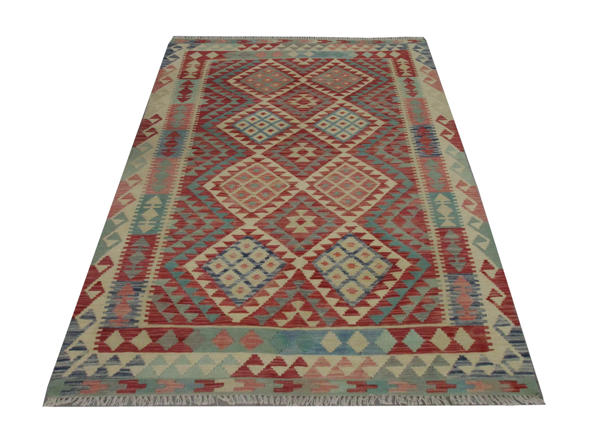 This sophisticated geometric kilim is a new traditional Afghan area rug woven by hand in the early 21st century. The central design is bold and beautiful, featuring a repeating diamond geometric pattern woven in pink, blue and beige accents, framed