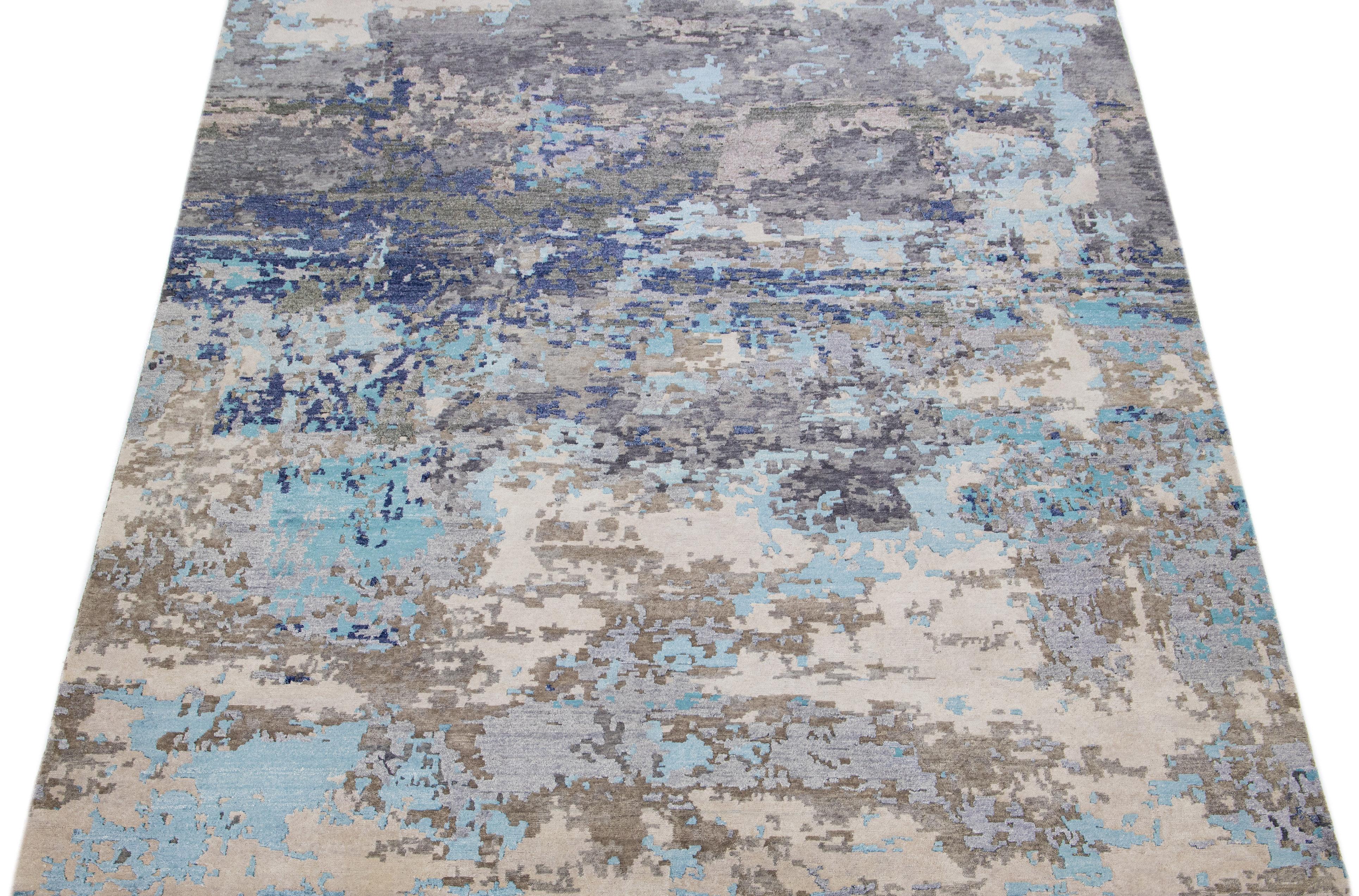 This Indian wool and silk blend rug features a light gray field with an abstract pattern detailing blue, brown, and beige colors. Its composed materials provide robustness and longevity, while its ornamental design infuses any room with