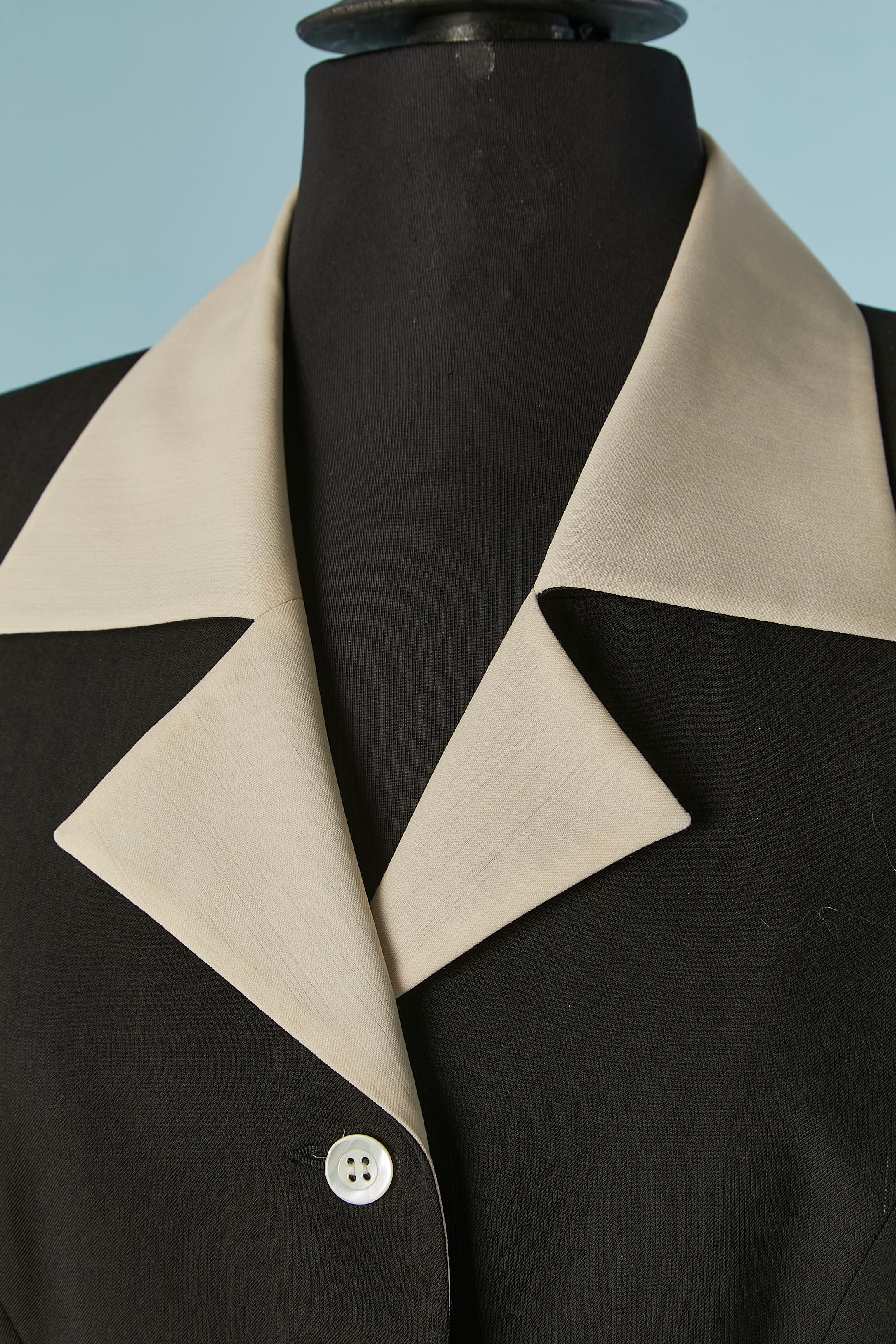 Chaqueta de lana negra de un solo pecho con cuello blanco roto y lazo . Forro de seda con lunares. 
Cierre de botón y ojal en el centro delantero + En los puños. Medio cinturón en la espalda con lazo. Hombrera.
TALLA 38 (Fr) M 