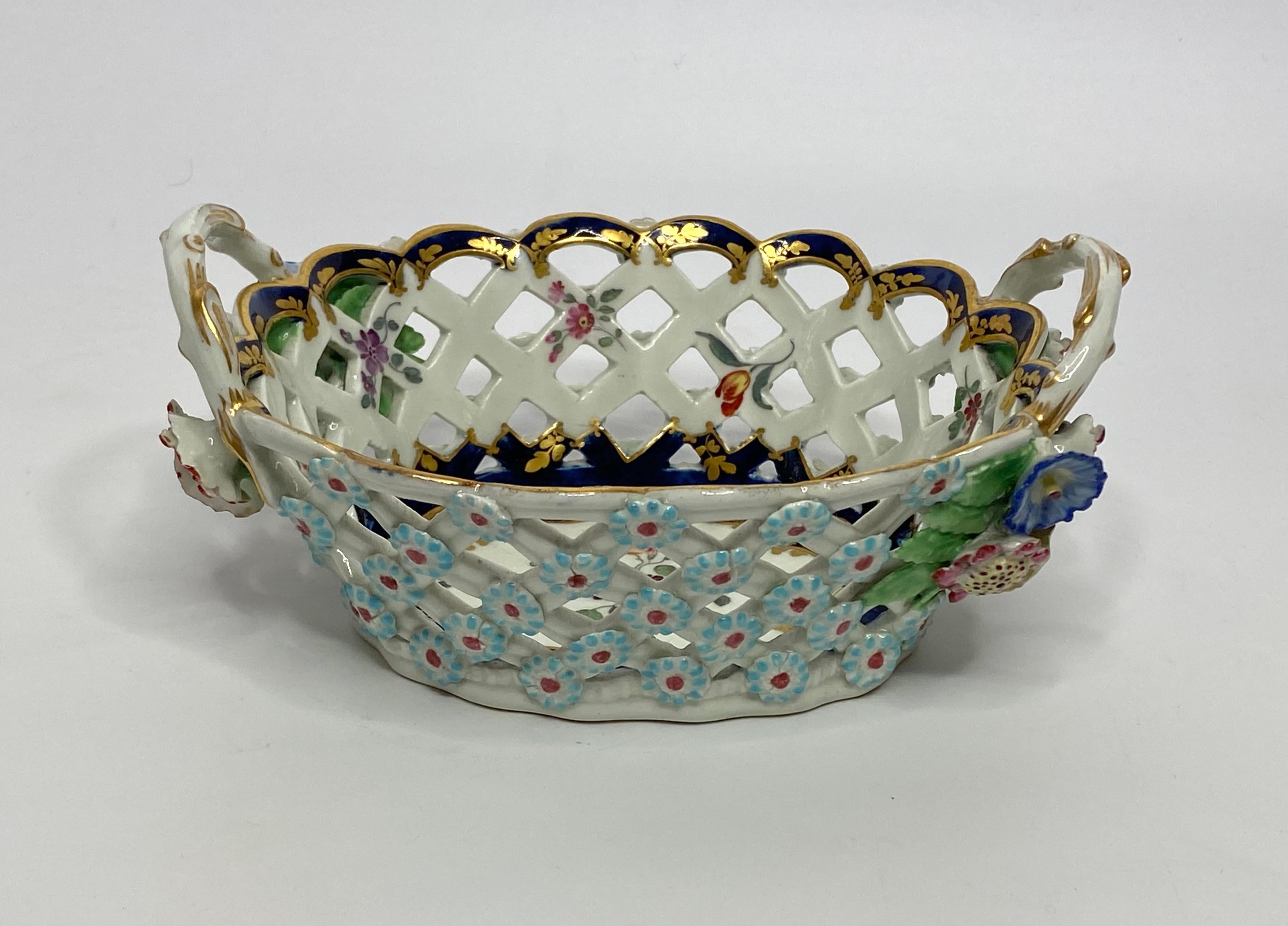 A fine and rare Worcester porcelain chestnut basket, c. 1770. Hand painted in the London workshop of James Giles, with a a spray of flowers, within an elaborate gilt scroll and flowered panel, on a underglaze blue scale ground. The lattice work,