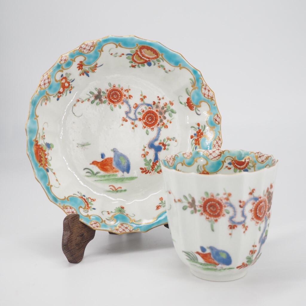 Worcester fluted coffee cup & saucer, in the 'Quail' pattern, with unusual border which brings together Rococo scrollwork and Kakiemon foliage, cup with entwined double handle. 

Fretted square mark on cup. 

Circa 1775.