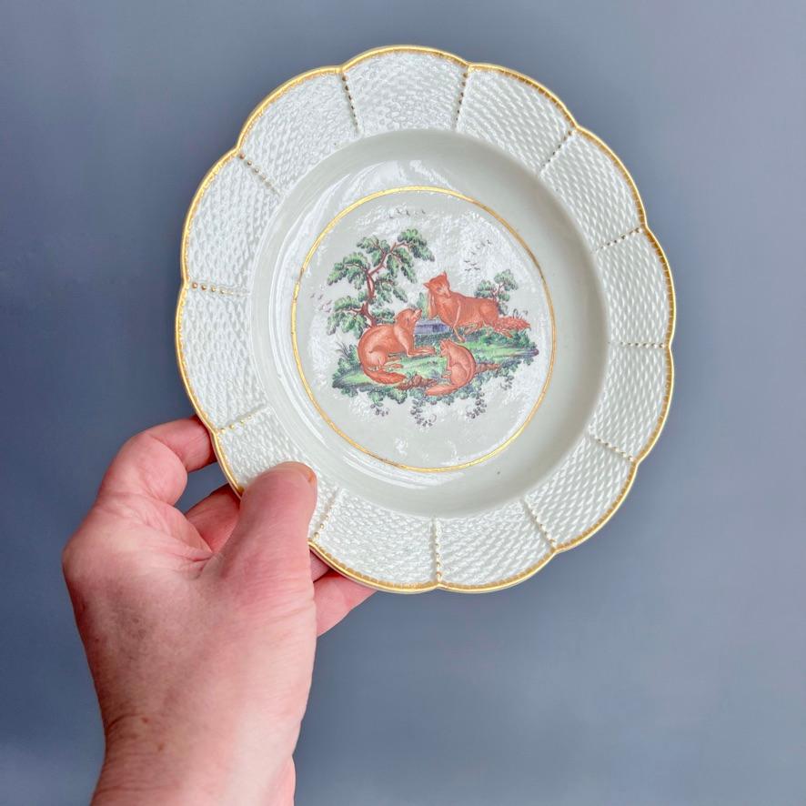 This is a very rare deep plate made by Worcester around 1780. The plate has a basket weave rim and a very charming image of an Aesop fable of three foxes coversing under a large tree, one of them clearly having a flee problem. The image is painted