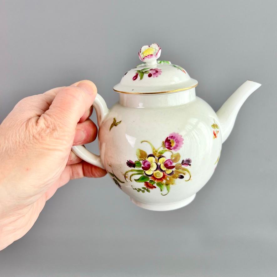 This is a very charming small teapot with cover made by the Worcester porcelain factory in about 1770. The teapot is globular in shape, with a simple white ground and elegantly painted flower sprays. The finial of the cover is in the shape of a