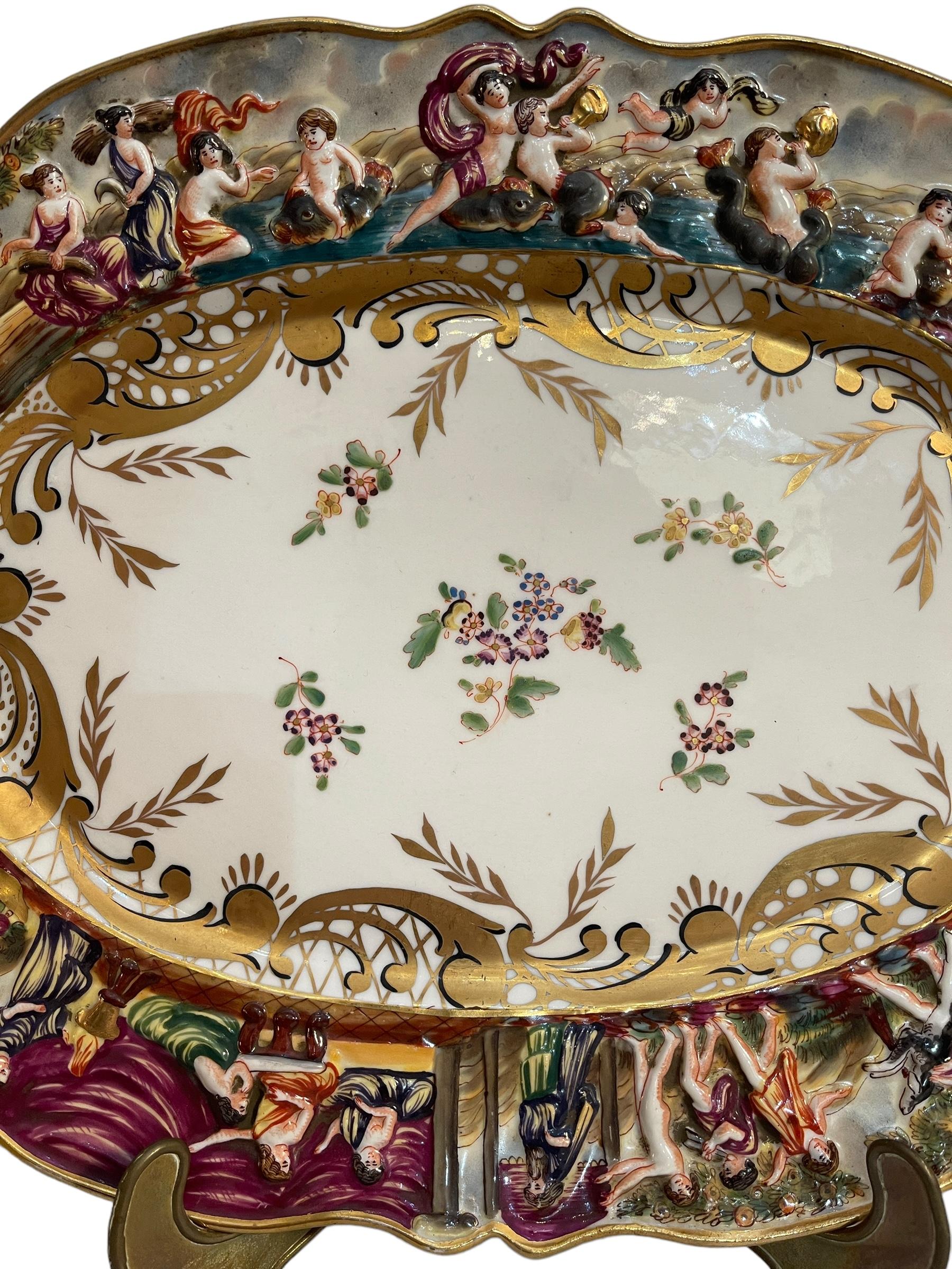 Refined ceramic plate, Capodimonte manufacture, branded.
The plate is worked in relief and painted by hand, it has a white base, golden decoration with floral motifs in the center and a rich workmanship along the contour, with figures, banquet