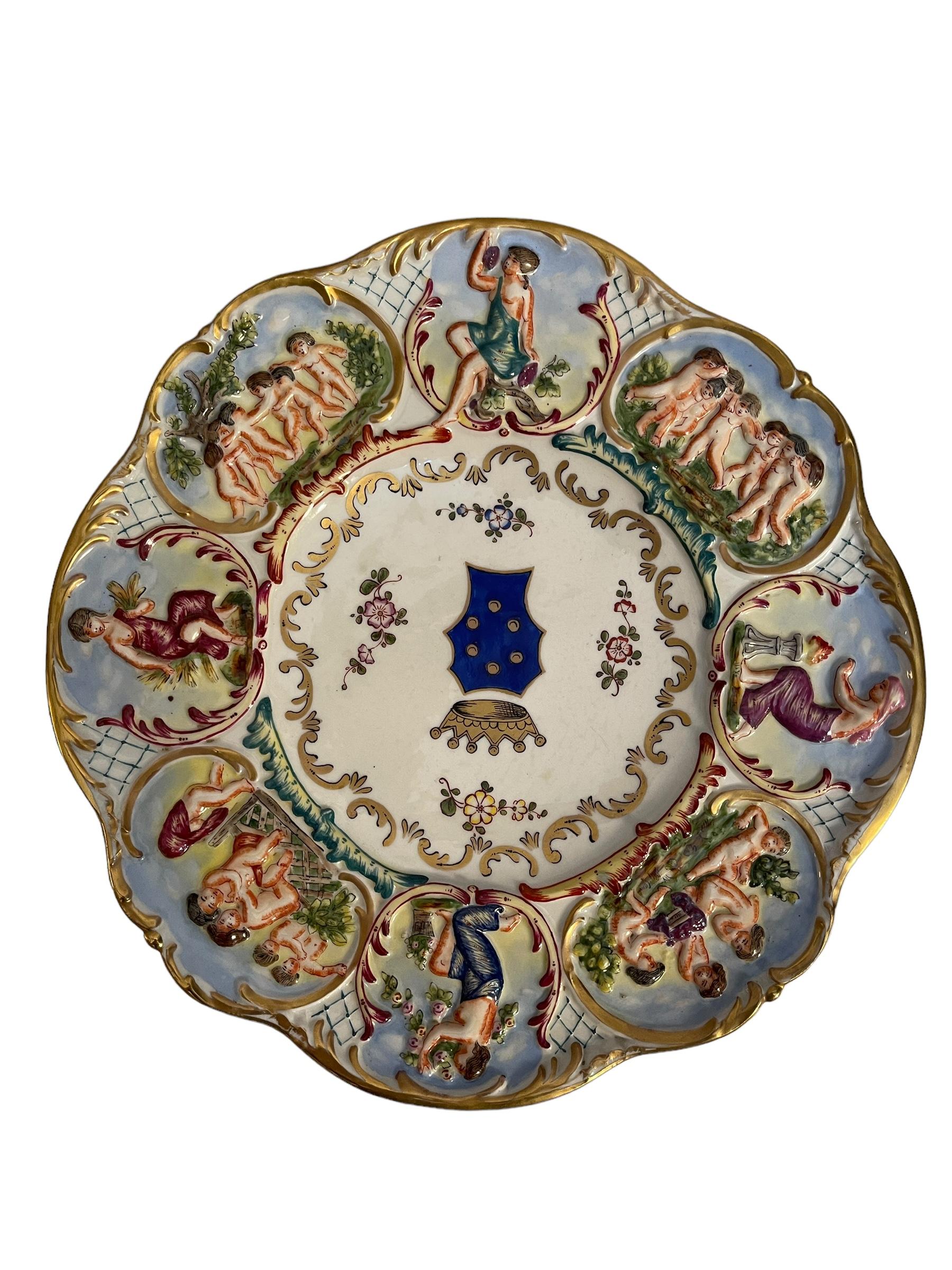 Die Platte ist in Relief gearbeitet und von Hand bemalt, es hat einen weißen Sockel, goldene Dekoration mit floralen Motiven in der Mitte, mit Wappen, und eine reiche Arbeit entlang der Kontur, mit Figuren, Szenen des täglichen Lebens, die vier