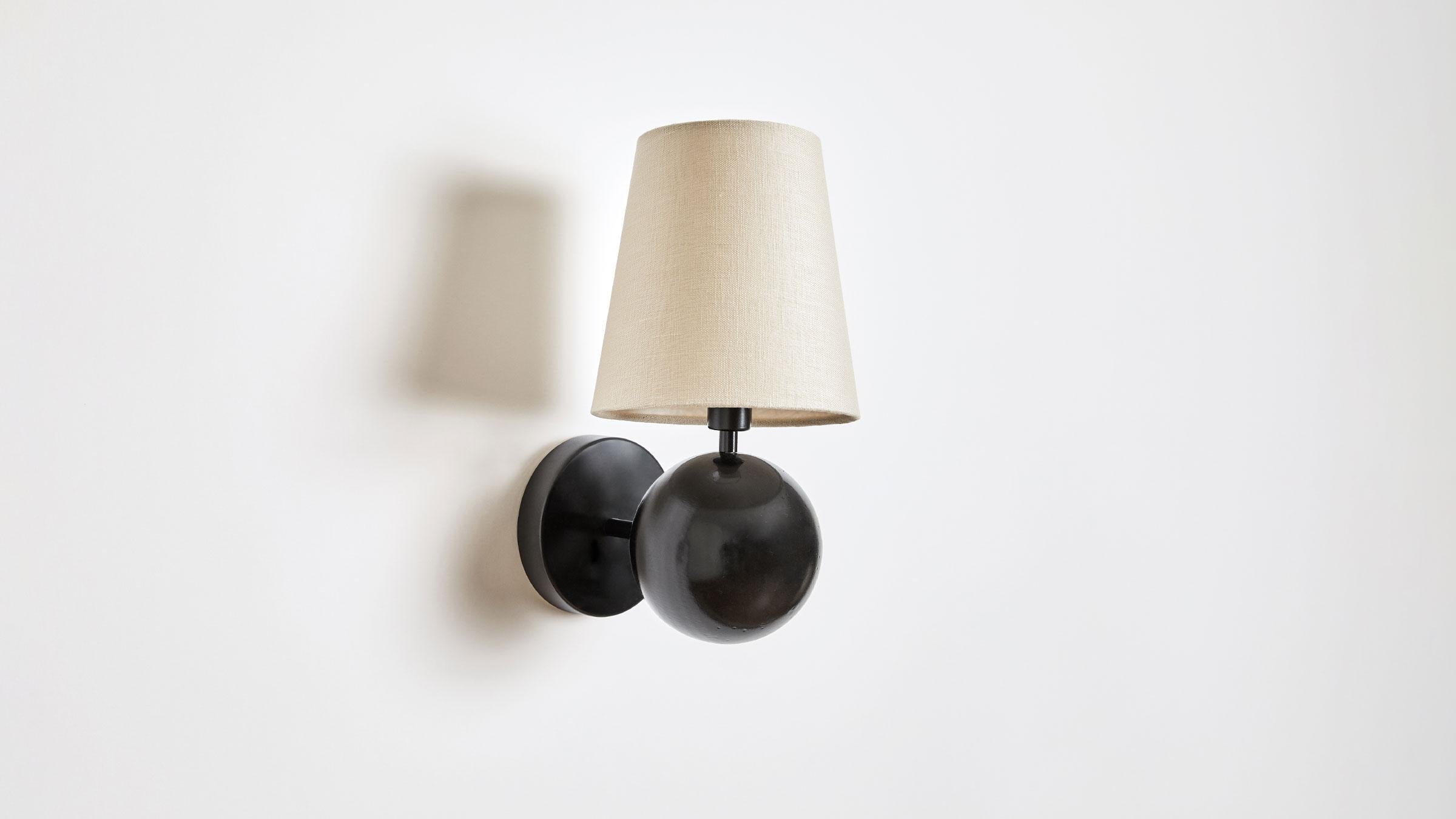 Bole positions a rotund form beneath a fabric shade, presenting a grounded yet buoyant composition for the wall. Available in White or Black Enamel, each version provides the perfect punctuation in any room. Made in the USA. UL Listed. Damp rated