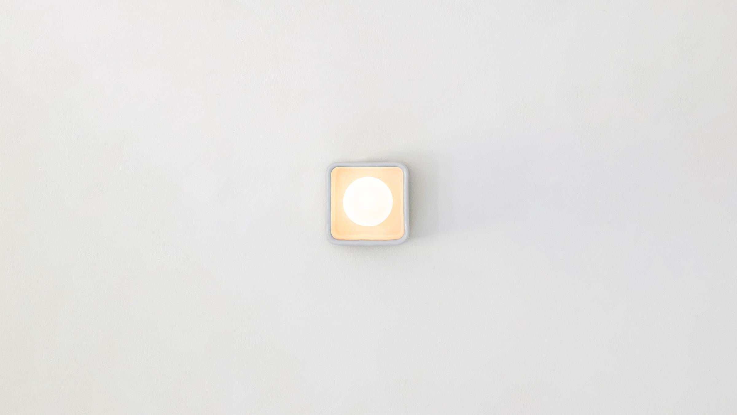 The Brick I is a modern interpretation of the Classic vanity light, celebrating the dialogue between the handmade and the serial. A cast earthenware base hand-glazed in soft white frames a matte opal globe, suggesting a hollowed brick cradling a