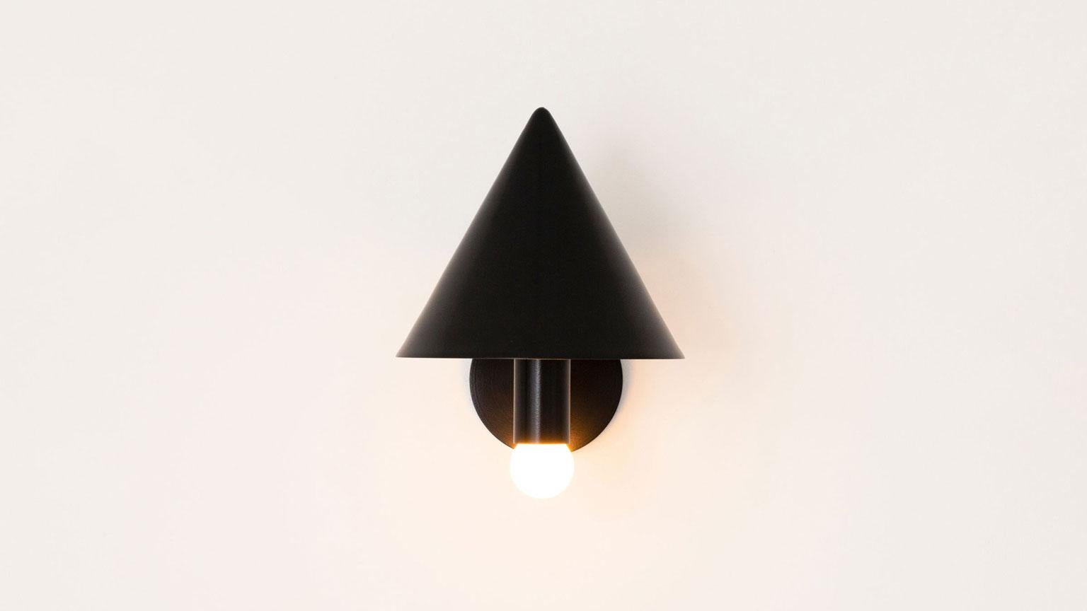The Canopy Sconce deconstructs the conventional wall sconce into a series of expressed, geometric relationships. A bold conical shroud rises above a softly glowing bulb creating a canopy of diffused reflection. UL Listed. Damp Rated upon request.