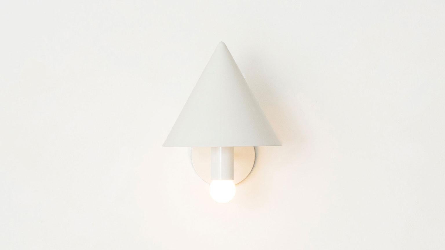 The canopy sconce deconstructs the conventional wall sconce into a series of expressed, geometric relationships. A bold conical shroud rises above a softly glowing bulb creating a canopy of diffused reflection. UL listed. Damp rated upon request.