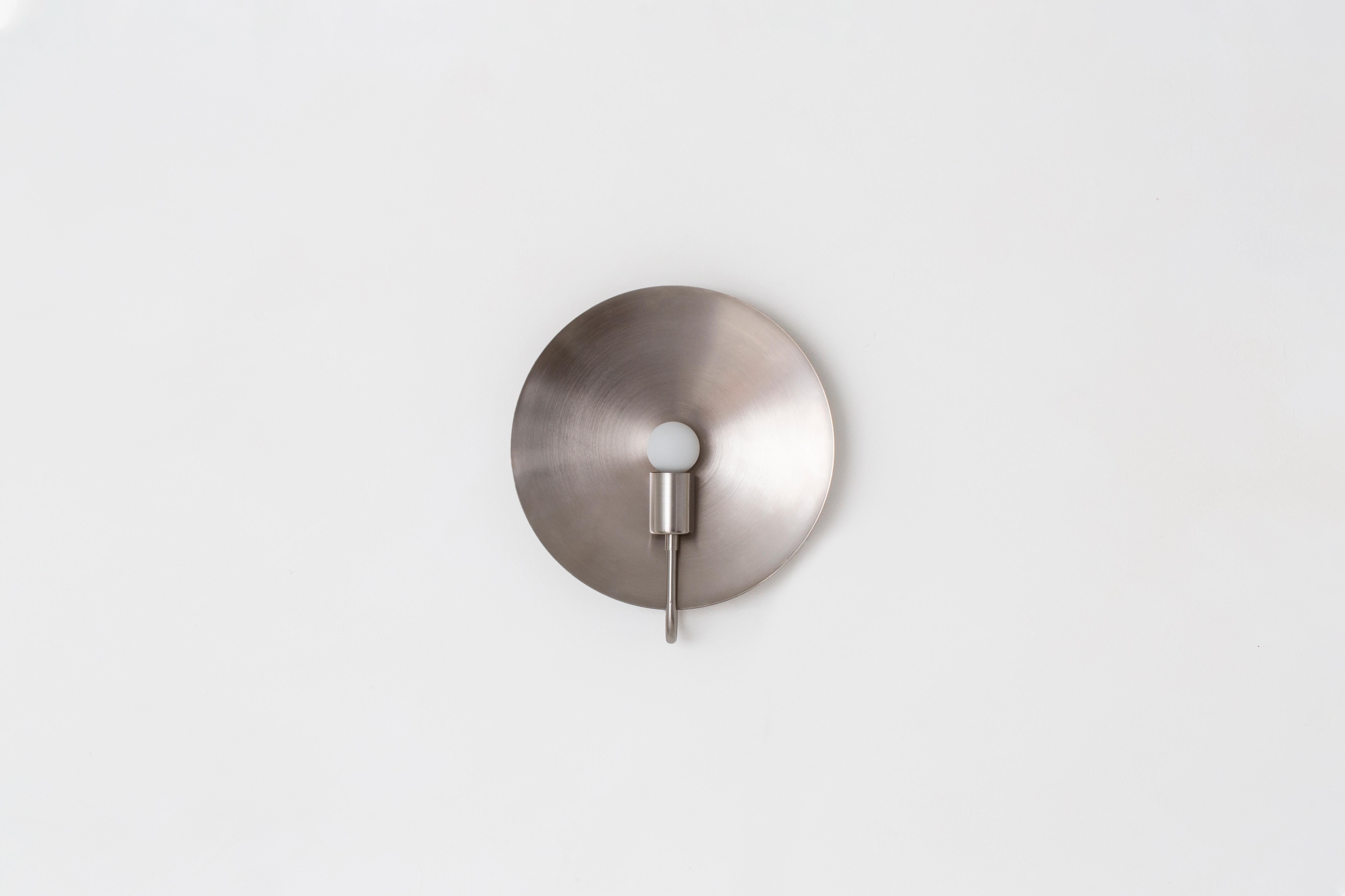 A fixed, wall-mounted version of our Classic Helios table lamp, this ADA compliant fixture is a sculptural object d’art. This sconce celebrates the celestial while maintaining a minimal footprint. A monumental spun-metal disc amplifies the glow from