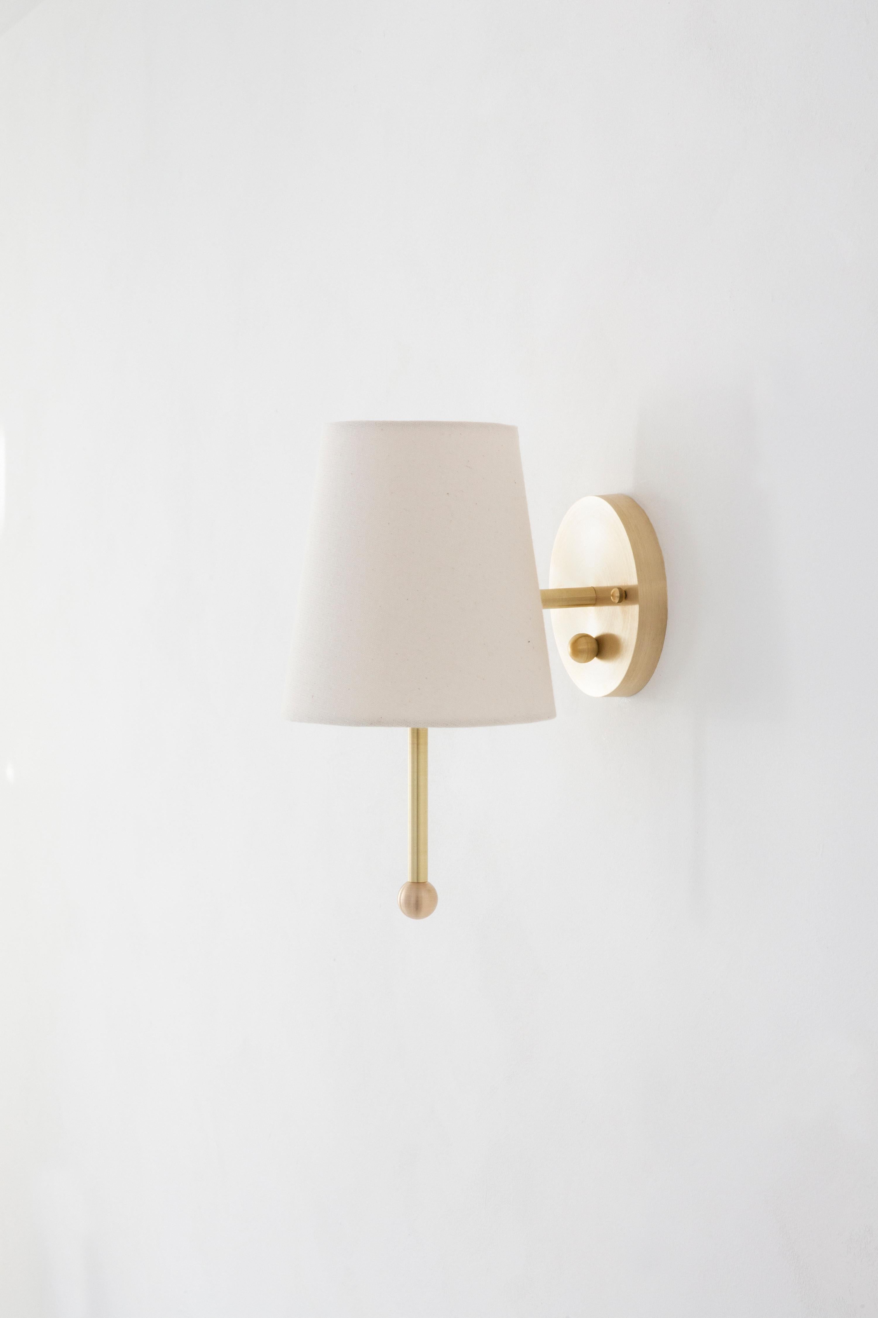 The house sconce is our take on the Classic shaded sconce typology made modern thanks to an unexpectedly playful spirit. The adjustable fixture can be pivoted as a whole, to create a graphic beam of light against the wall. Available in hewn brass