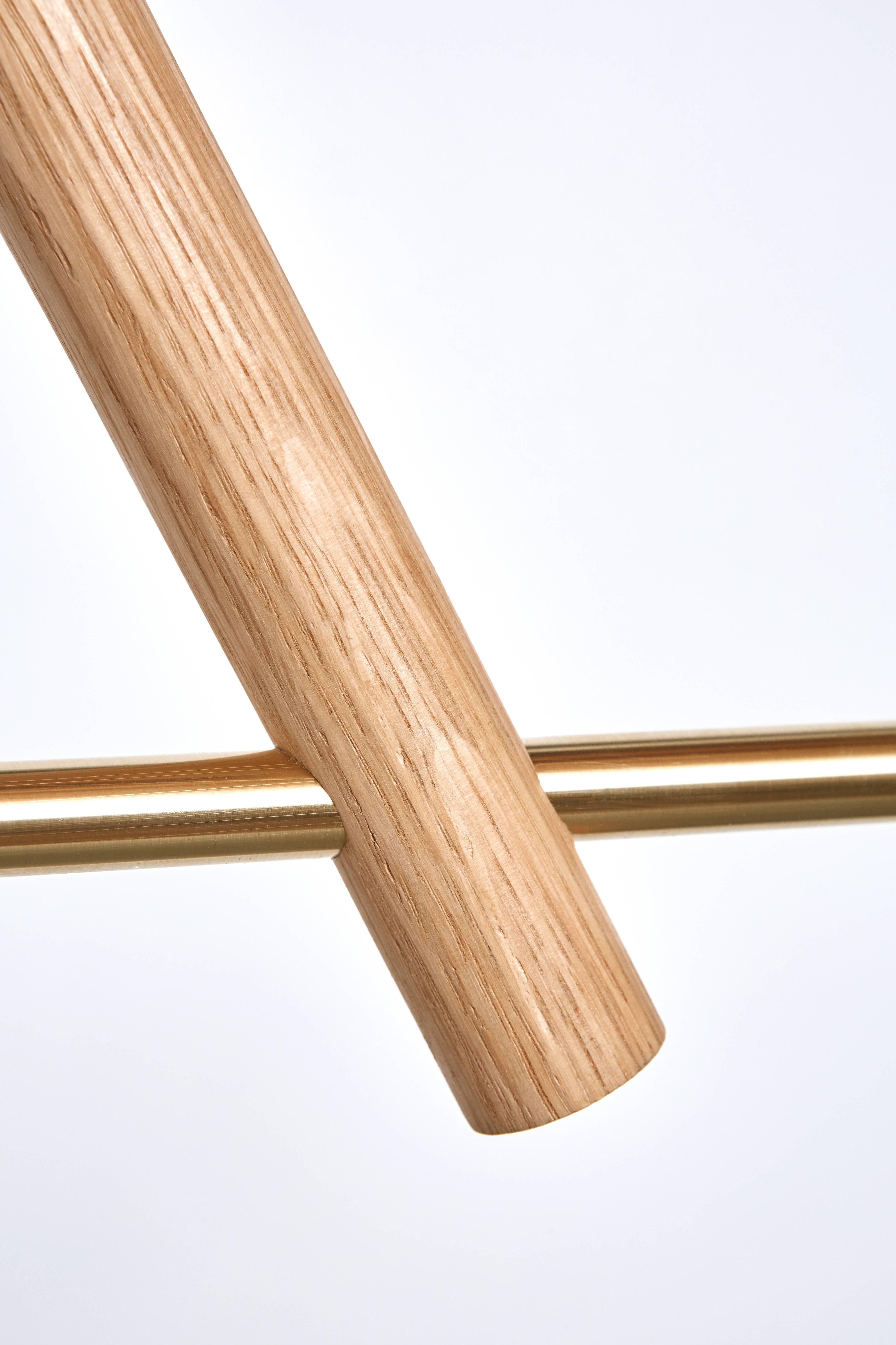 Le lustre lodge deux poursuit le jeu de l'ossature bois et de la structure métallique à l'échelle d'un lustre directionnel. Une structure rigide en bois supporte deux tubes délicats qui éclairent deux sources lumineuses à chaque extrémité du