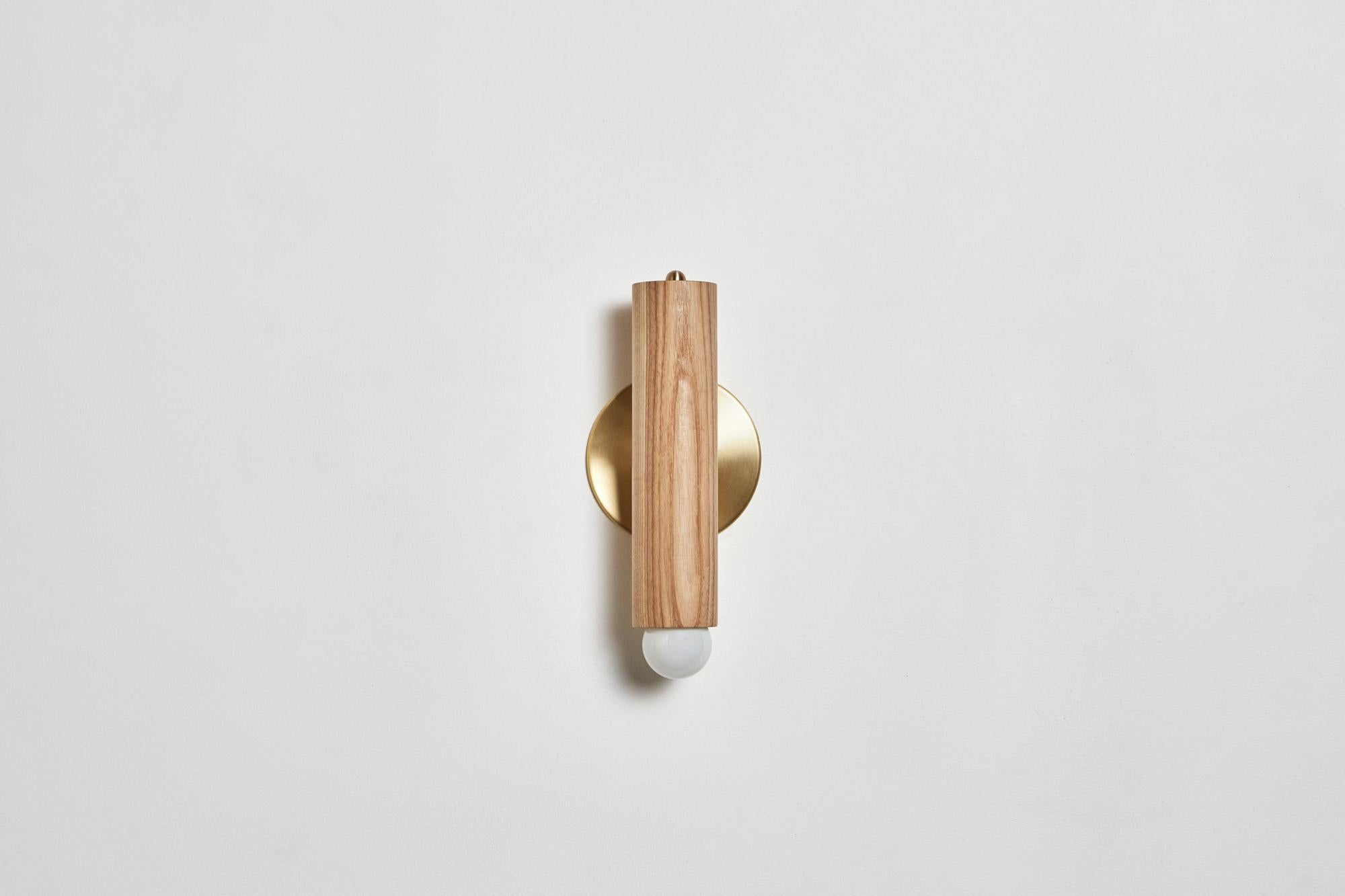The lodge sconce is composed of a singular wooden column mounted on a metal back plate. The fixture swivels from side to side, directing light from a softly glowing bulb.

Shown in natural oak and hewn brass. Dimmer located at top of sconce.