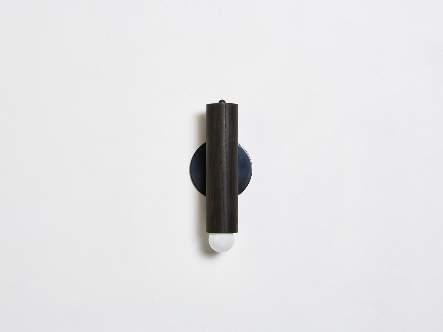 The lodge sconce is composed of a singular wooden column mounted on a metal back plate. The fixture swivels from side to side, directing light from a softly glowing bulb. 

Shown in oxidized oak and blackened steel. 
Dimmer knob located at top of